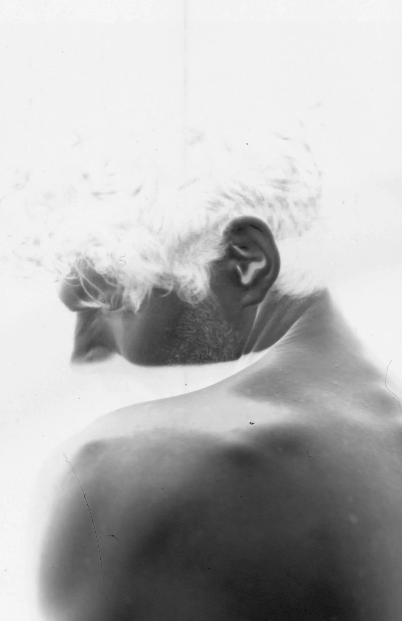 Black and white photograph of a person's head from a side profile with closed eyes and hair tied back, against a plain background.