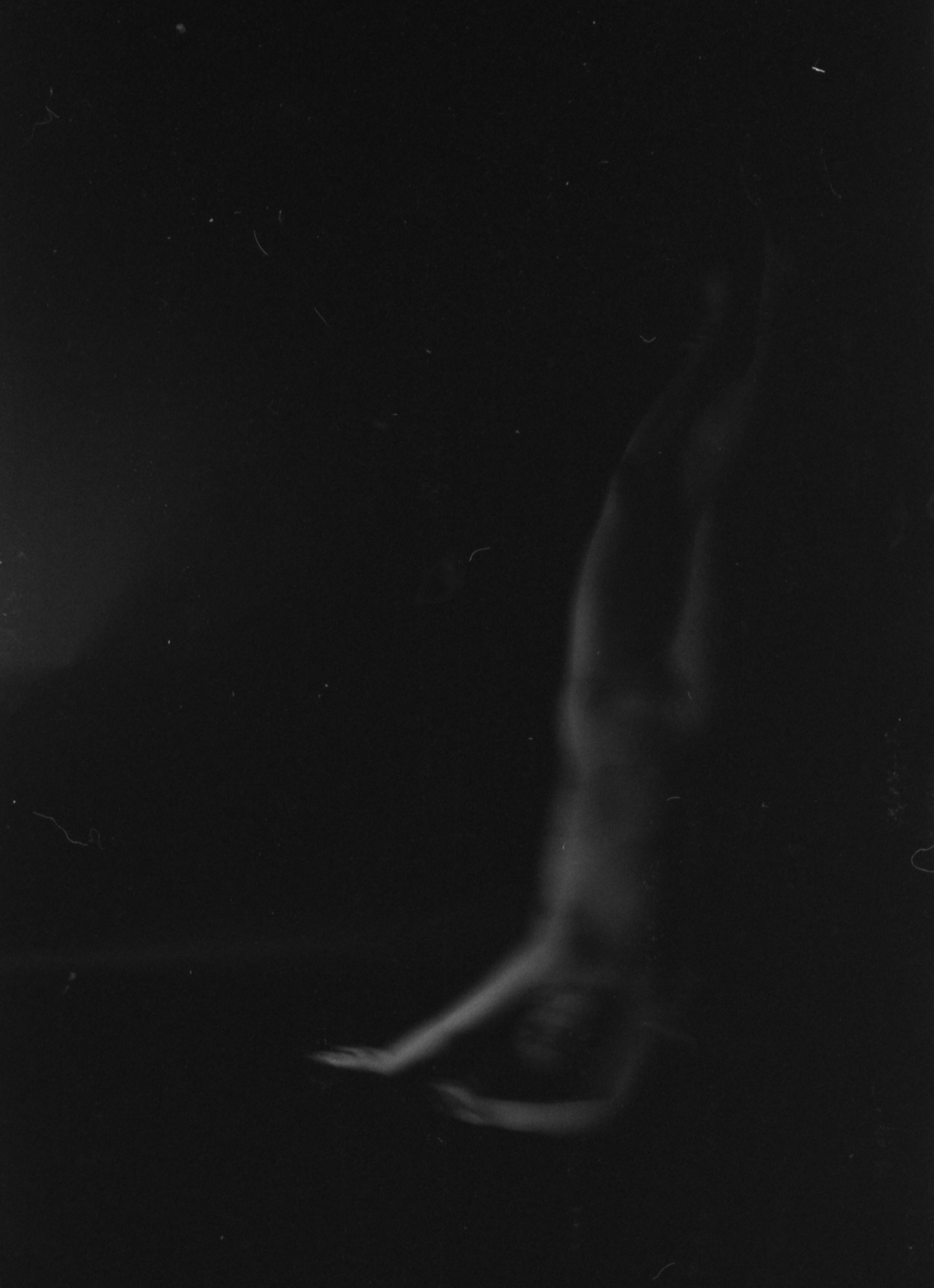 Black and white photo of a person's hand holding a cigarette or lit object, partially obscured by smoke.