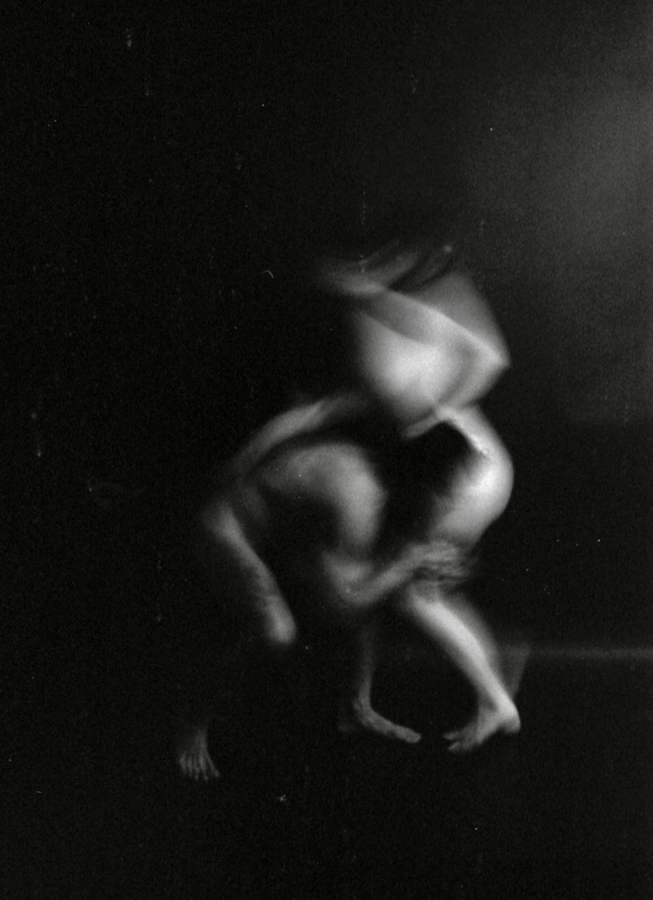 Black and white photo of a baby holding a pacifier, in a dark environment.