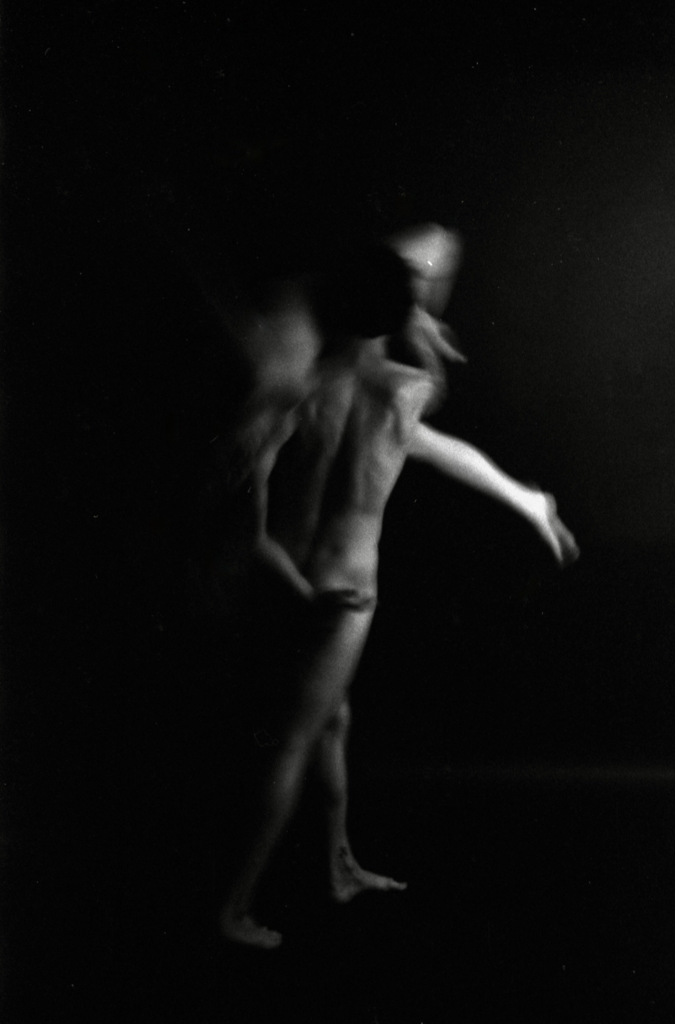 A black and white photograph of a person holding a small, possibly animal, facing downward. The background is completely dark, emphasizing the silhouette of the hand and the object being held.
