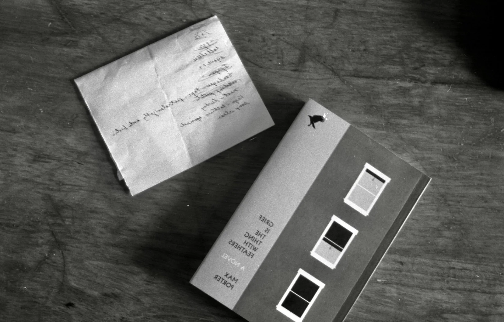 A notebook and a small note with handwritten text on a wooden surface.