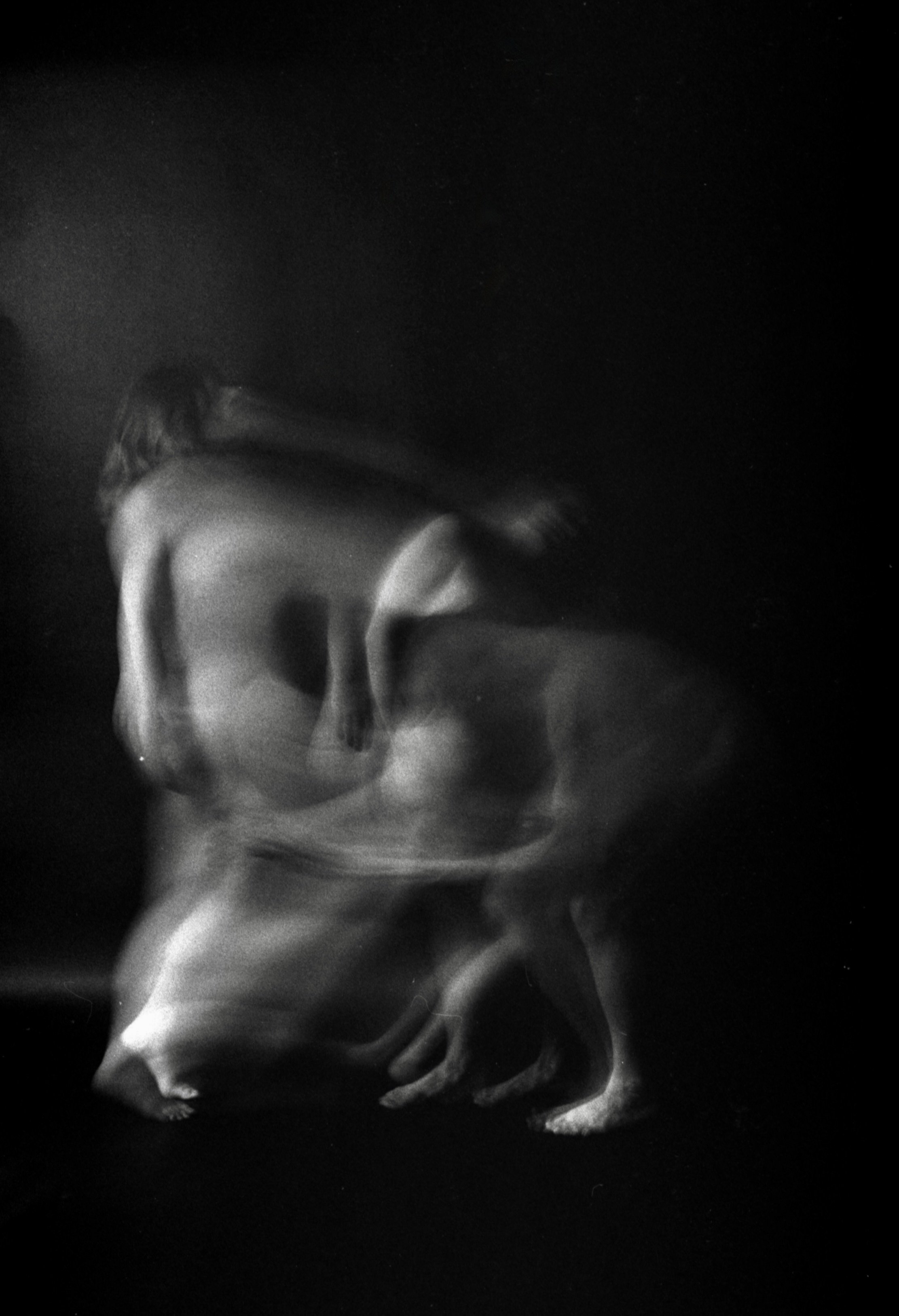 Black and white photograph of a figure with wings, seemingly floating or flying against a dark background with faint stars or specks of light.
