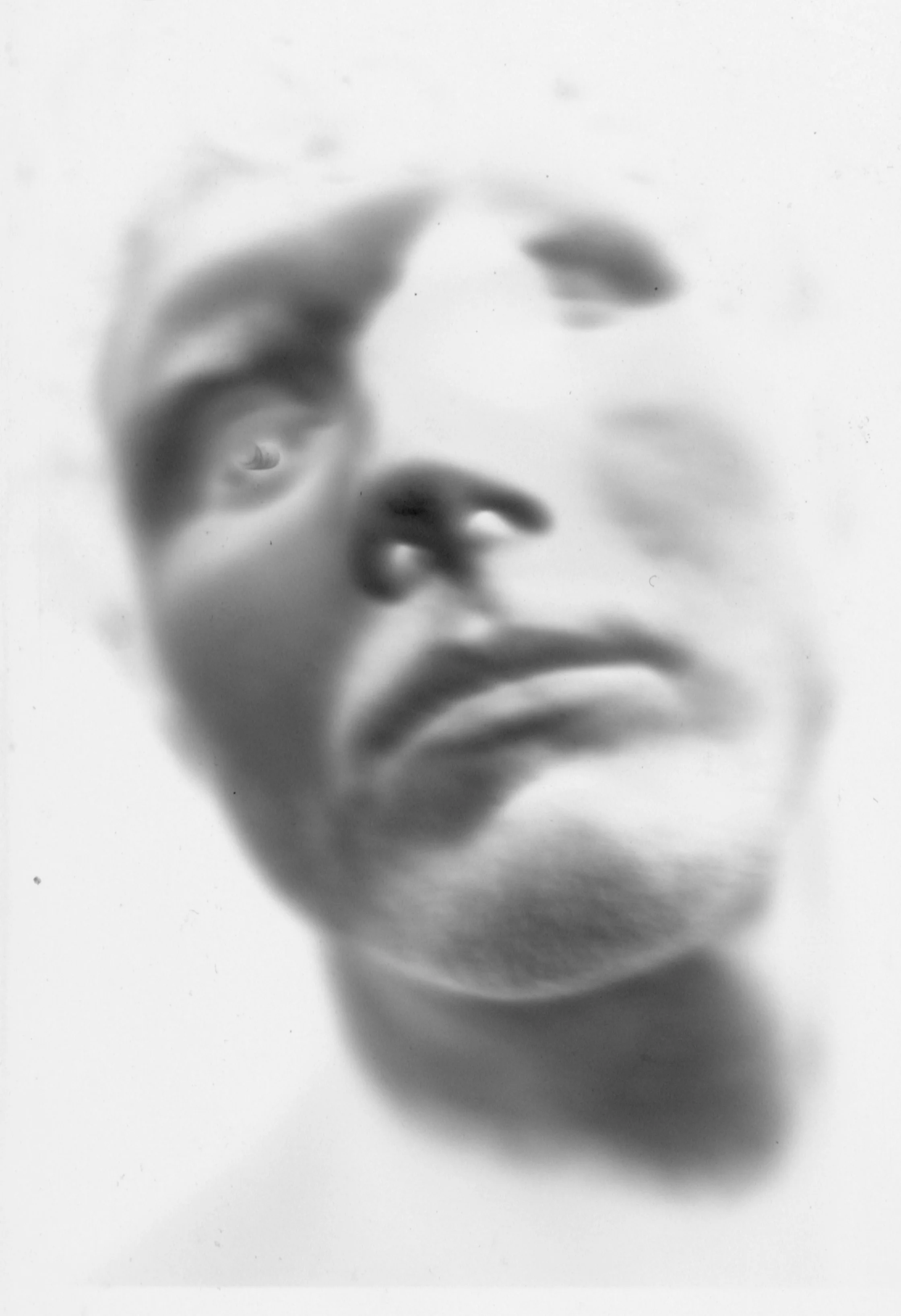 A blurred black and white close-up photograph of a person's face, with their hand near their chin and a nose visible.