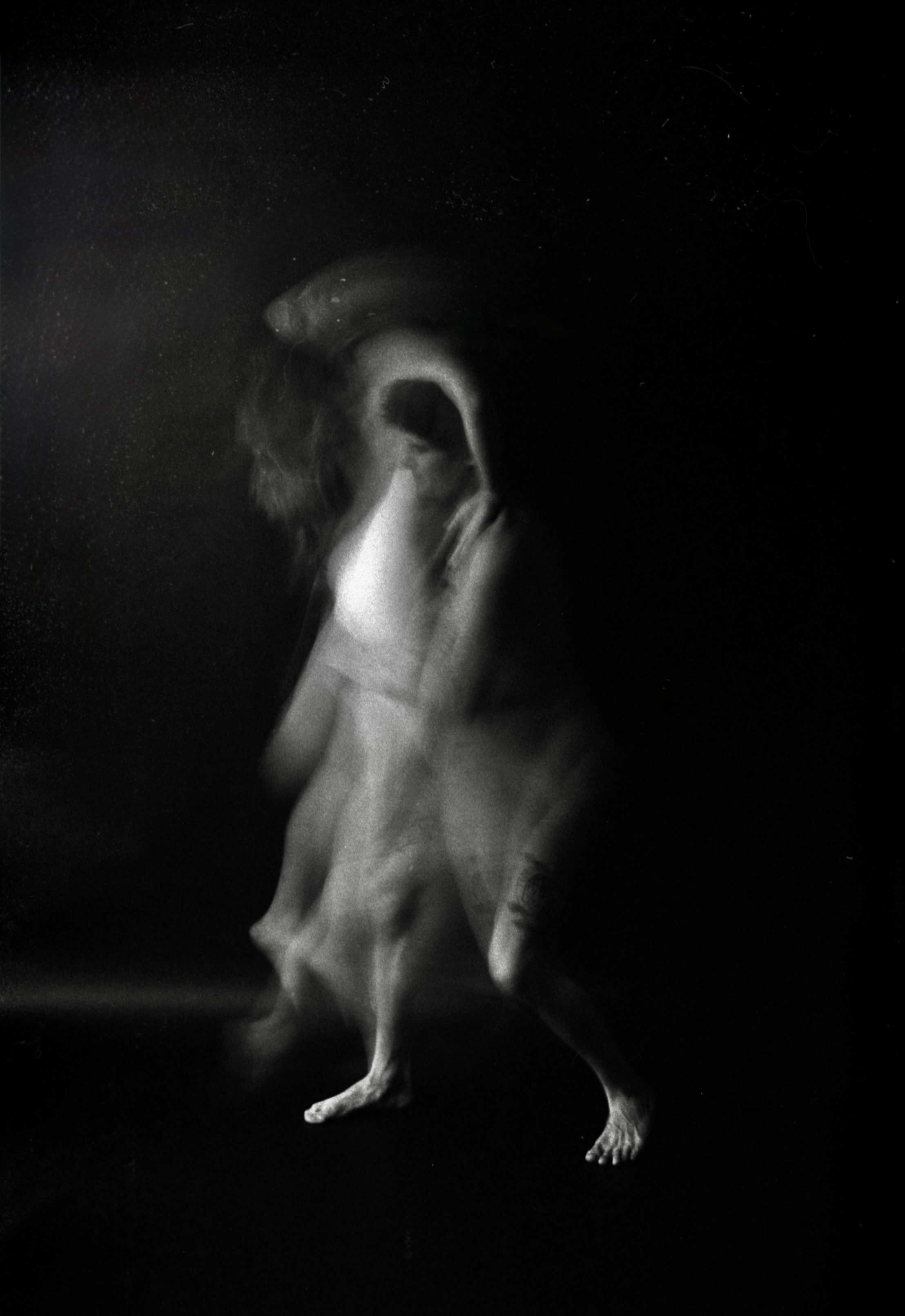 A black and white photo of a dog standing on its hind legs, with a dark background and some light highlighting its body and face.