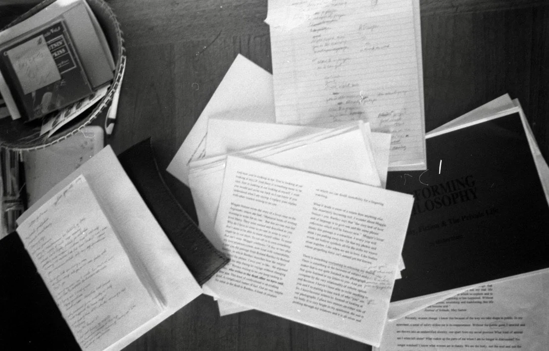 Various documents, papers, and books spread out on a desk, including a notebook, printed pages, and a book titled 'Forming Philosophy'.