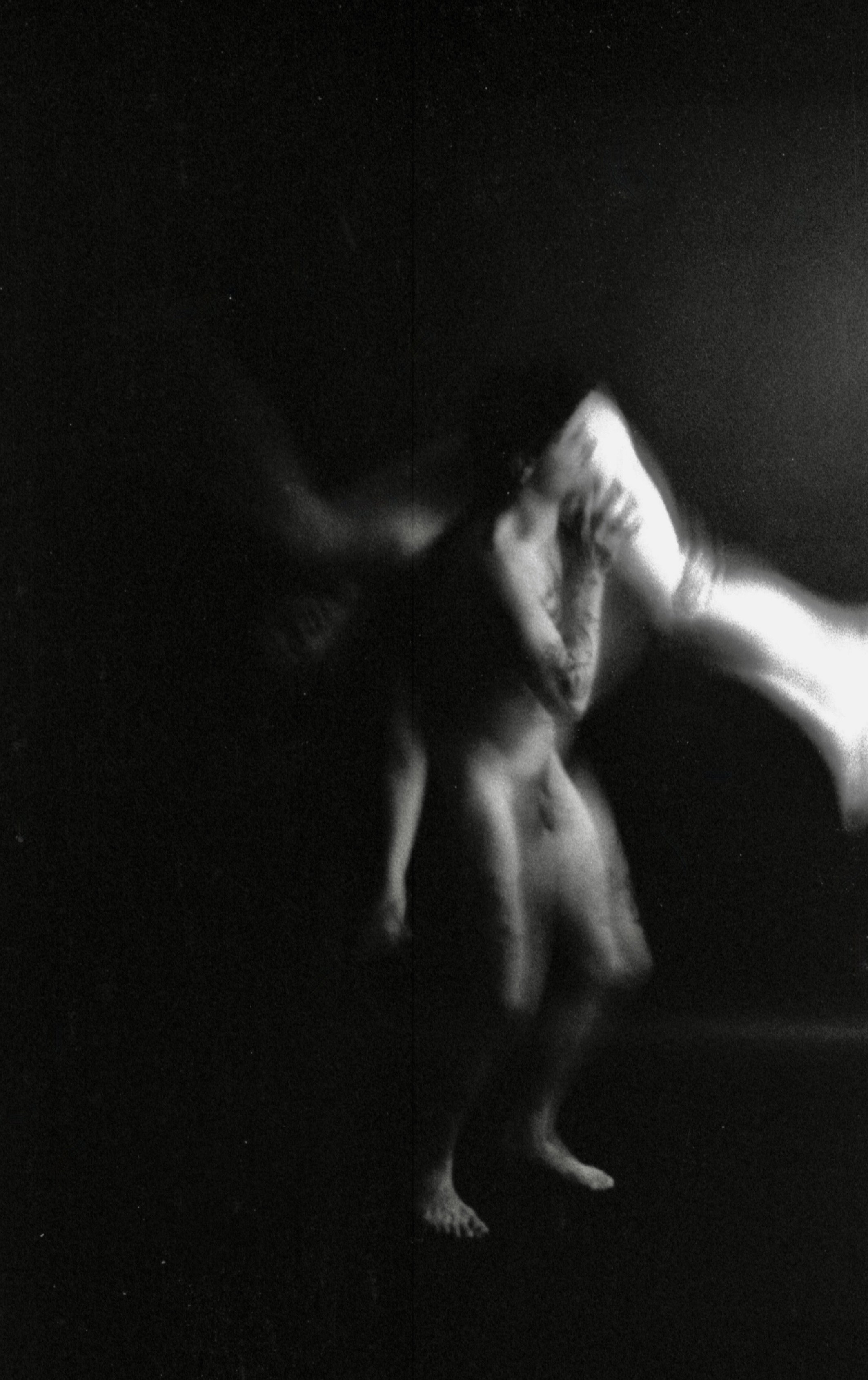 Black and white photo of a person standing in a dark area, with their eyes closed, head tilted back, and hands covering their face.