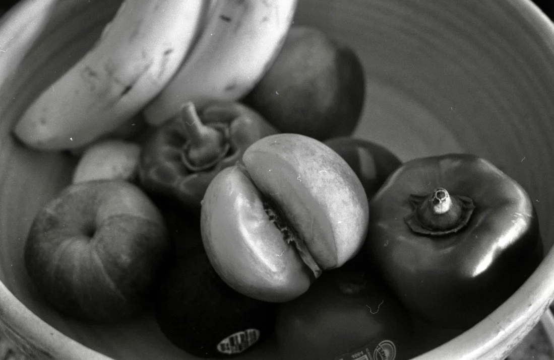 Black and white photo of assorted fresh fruits, including tomatoes and peppers, inside a bowl.