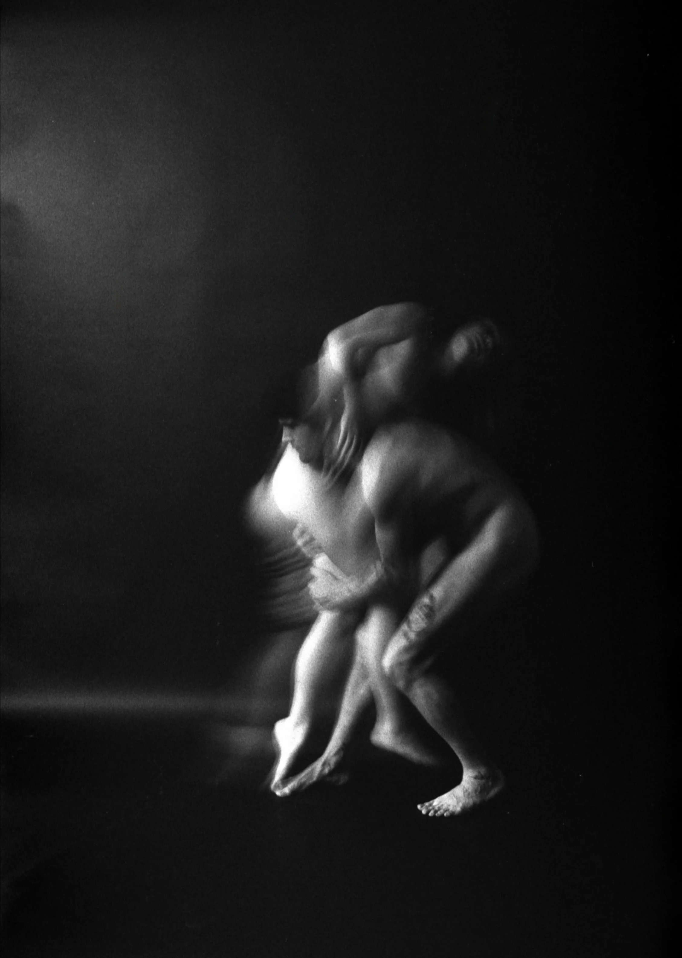 Black and white photo of a woman bending forward, her face near her bent knee, with her eyes closed and mouth open in an expressive pose.
