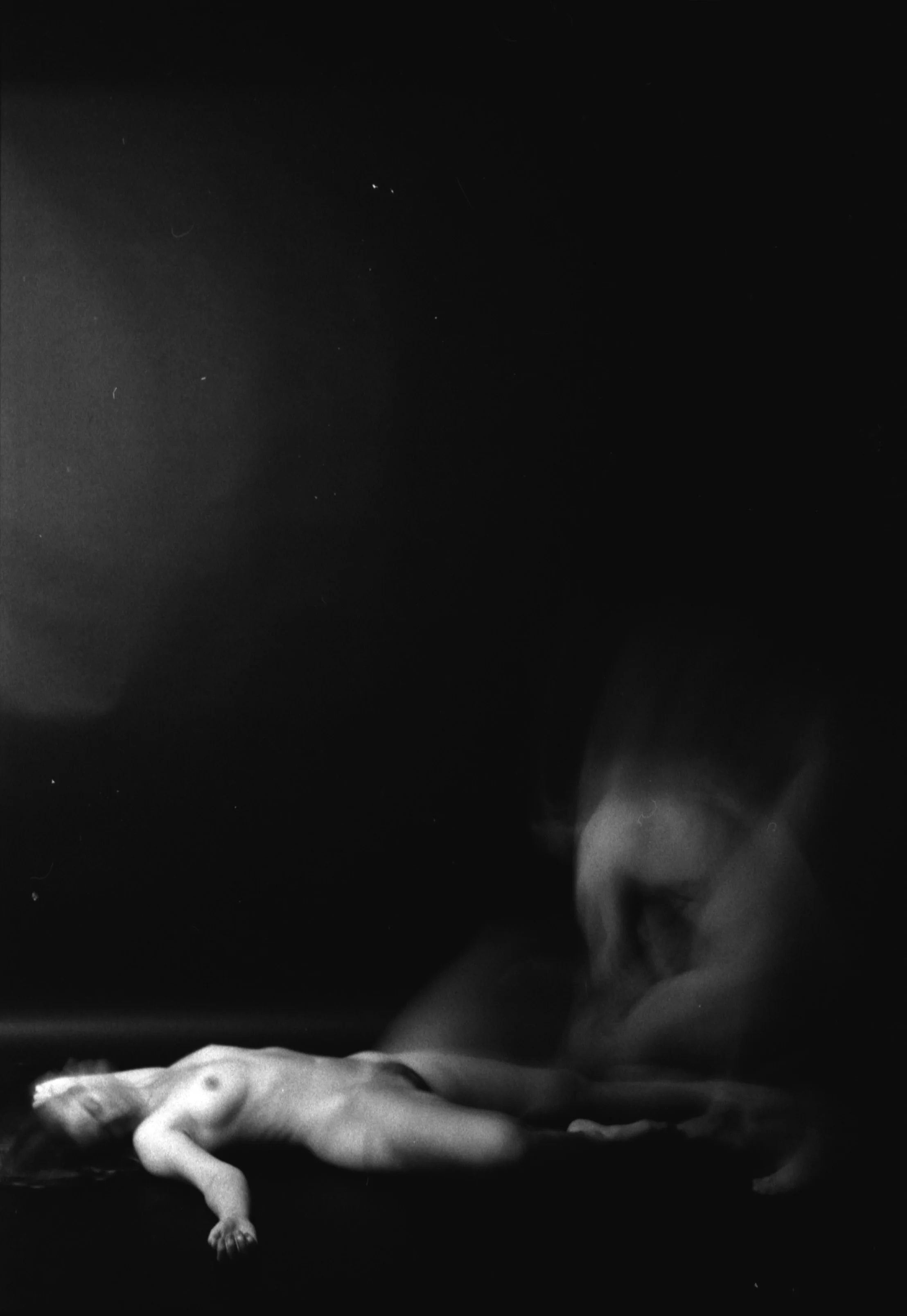 Black and white photo of a nude man lying on his side on a bed or surface, with his eyes closed and head resting on his arm.