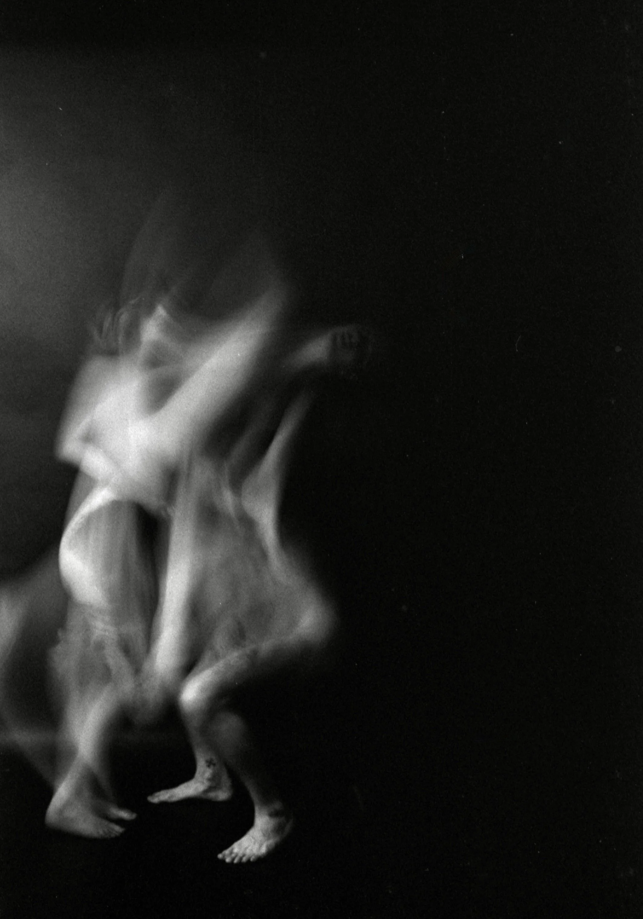 A black and white image showing a person with curly hair bending forward in a dark background.