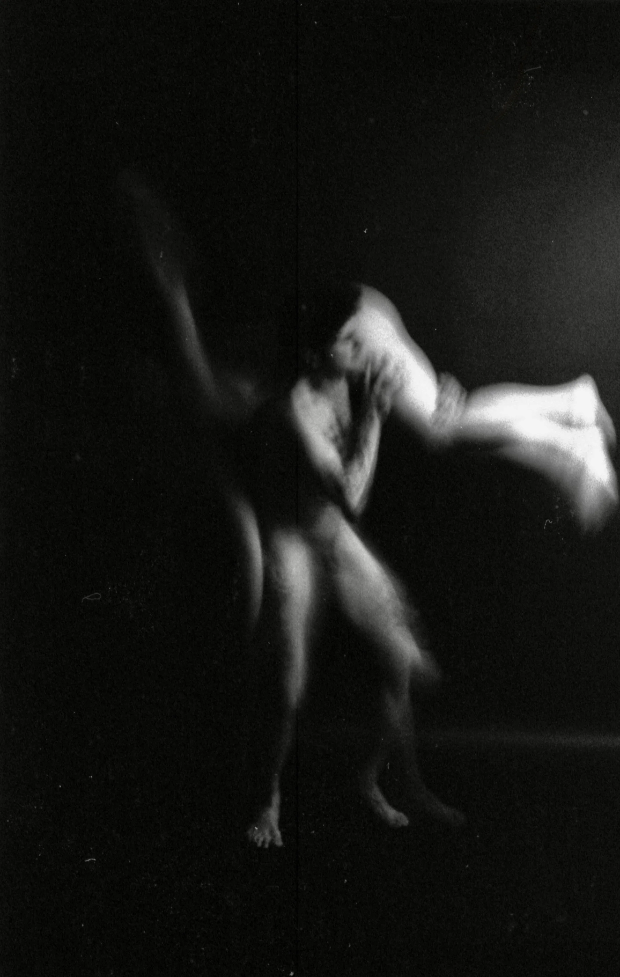 A black and white photograph of a person with long hair standing on a dark surface, holding a dog in their arms. The dog appears to be lying on the person's shoulder, with their face pressed to their arm.