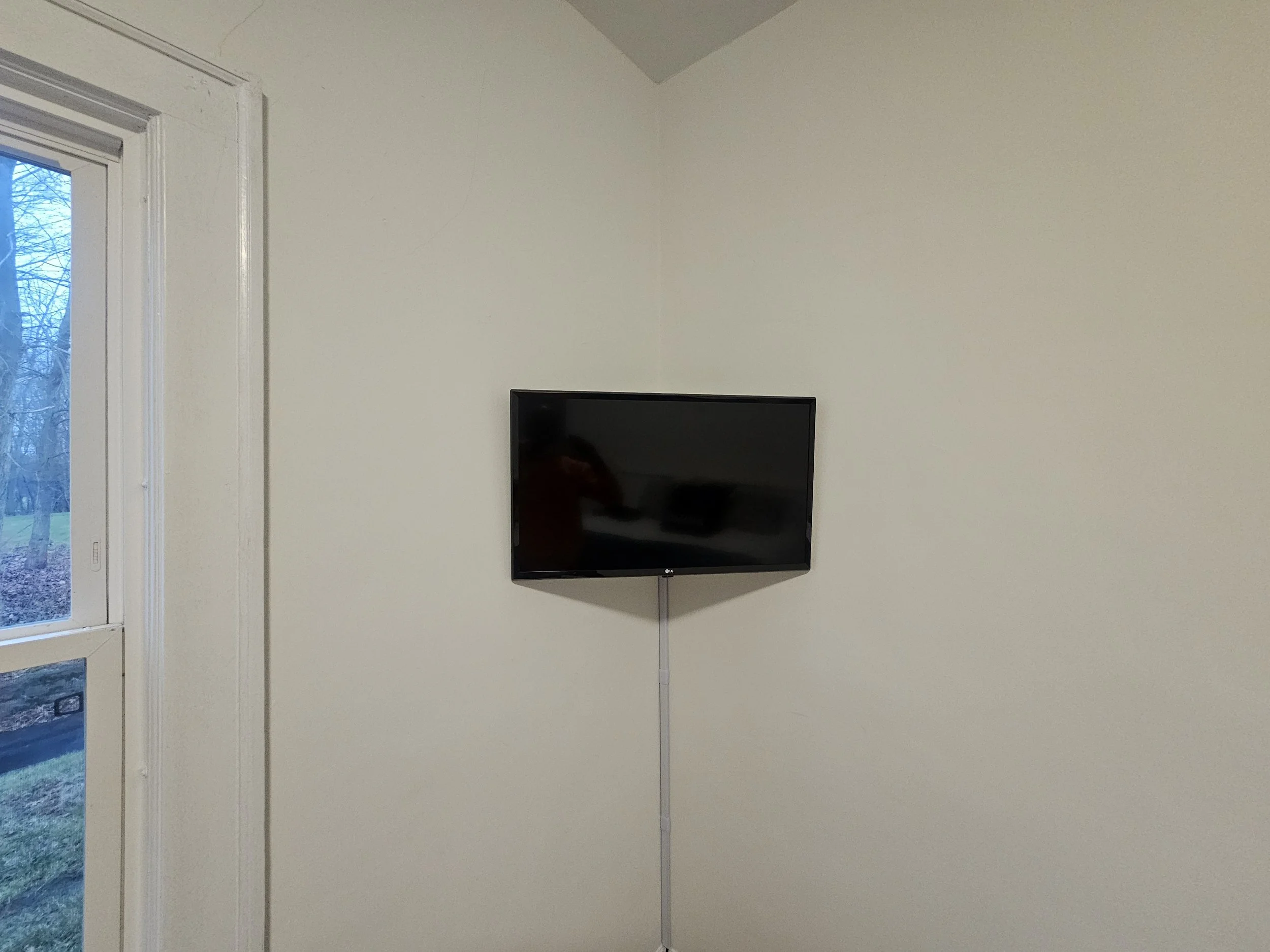 Flat-screen TV mounted on a white wall near a window.