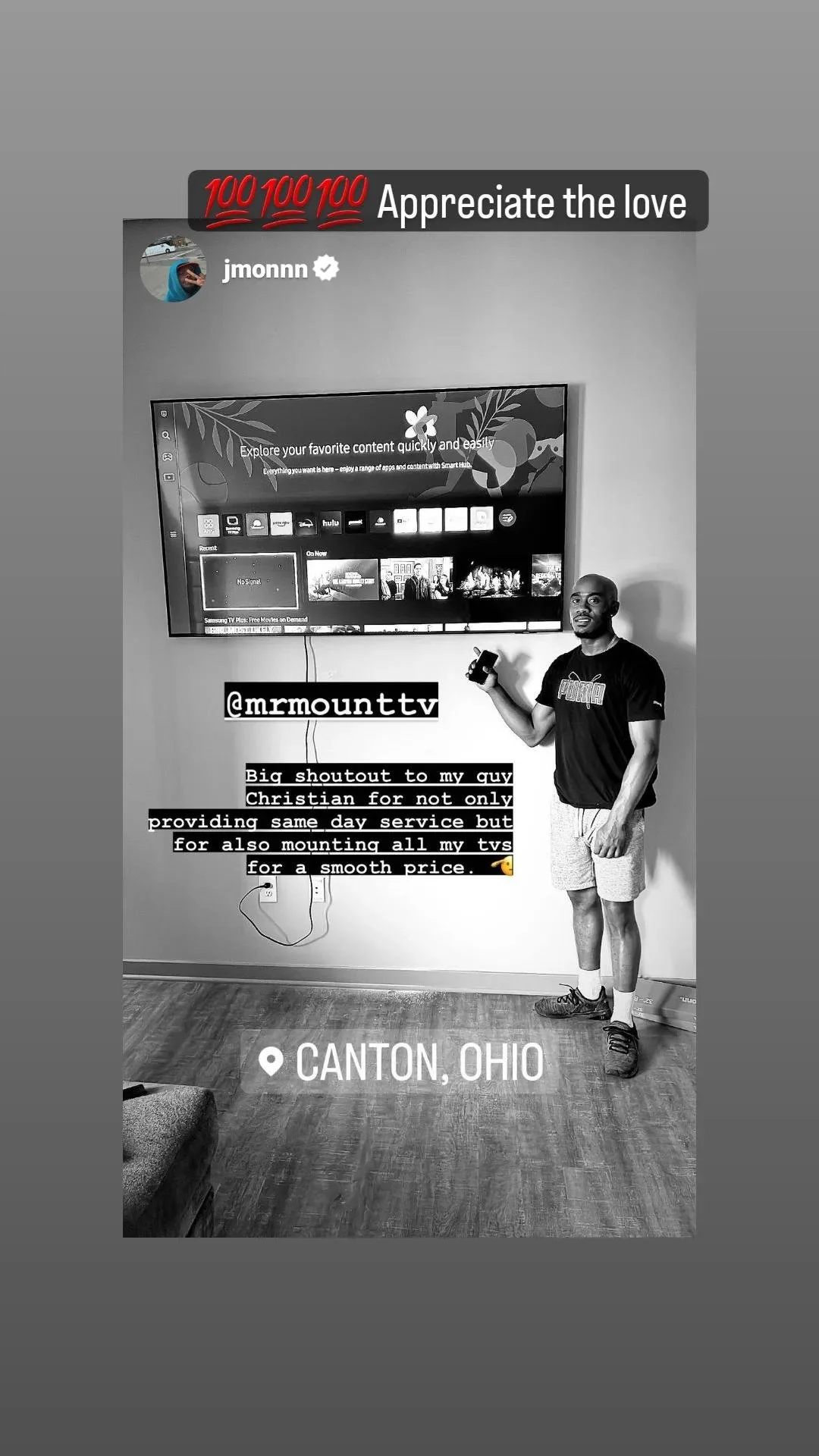 A man standing indoors in front of a large television mounted on the wall, holding a remote control, with a caption thanking a person named Christian for mounting multiple TVs at a good price. Text overlay indicates the location as Canton, Ohio, and 