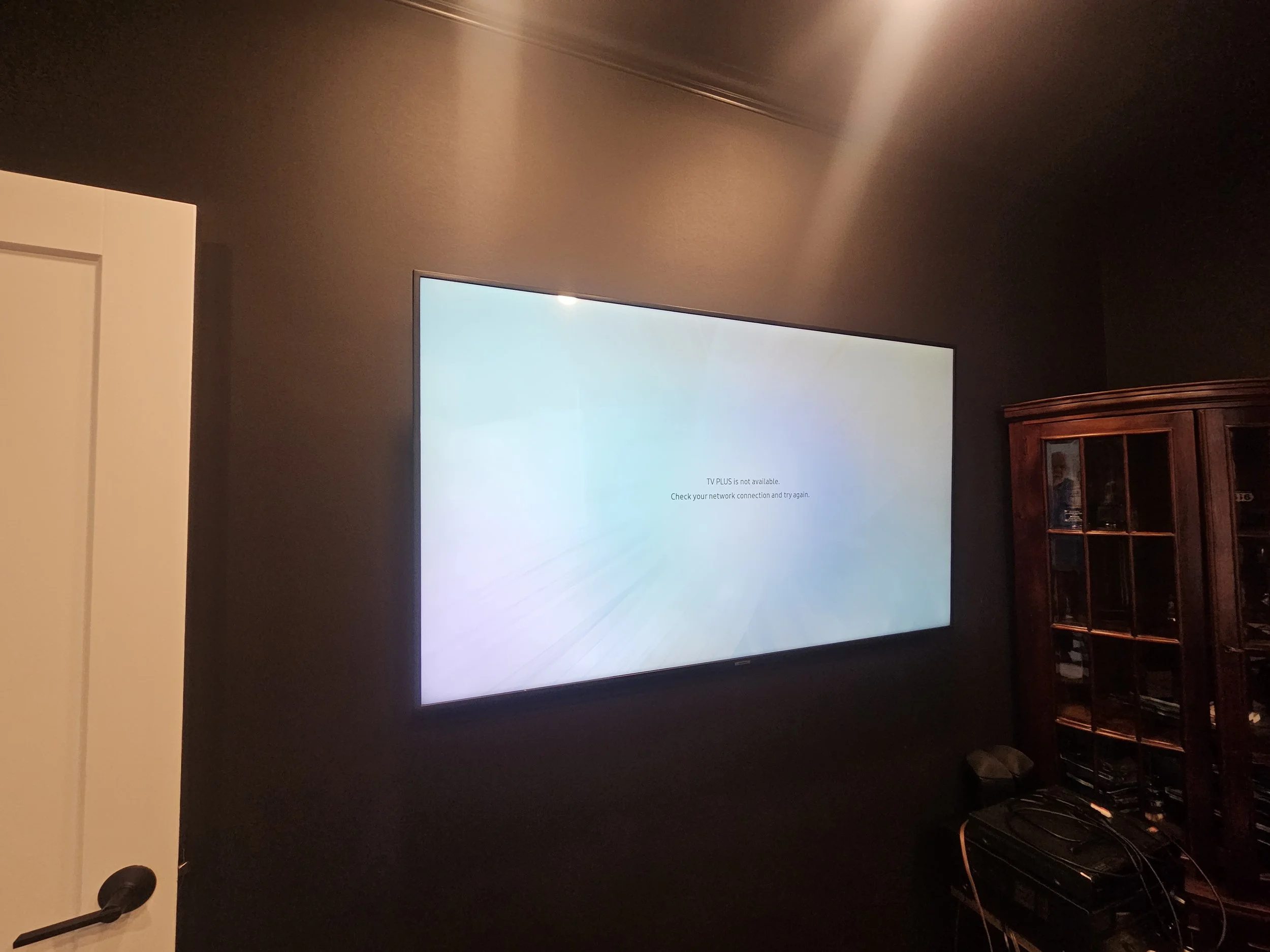 Flat screen television mounted on a dark wall displaying an error message: 'TV PLUS is not available. Check your network connection and try again.'