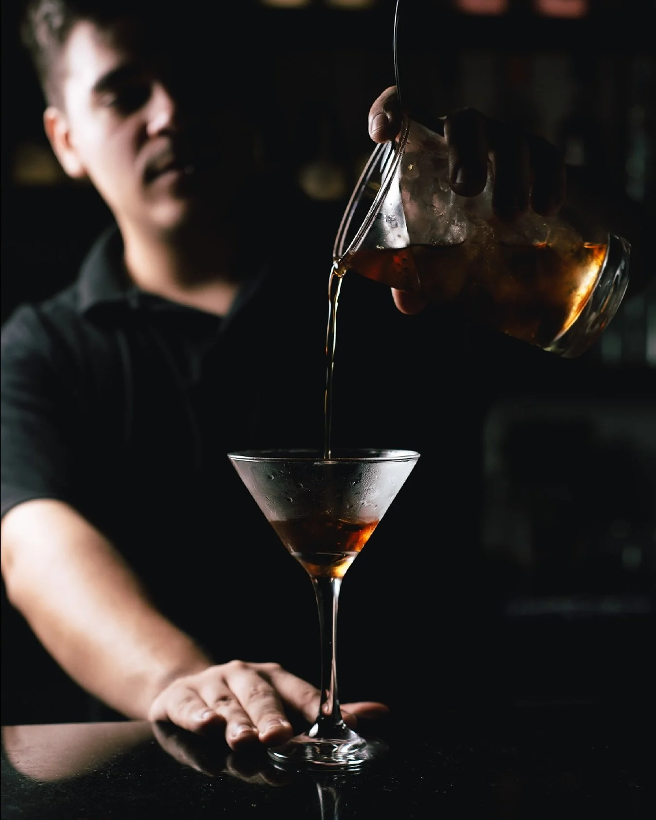 Un barman sirviendo un cóctel en una copa de cóctel en un bar oscuro.