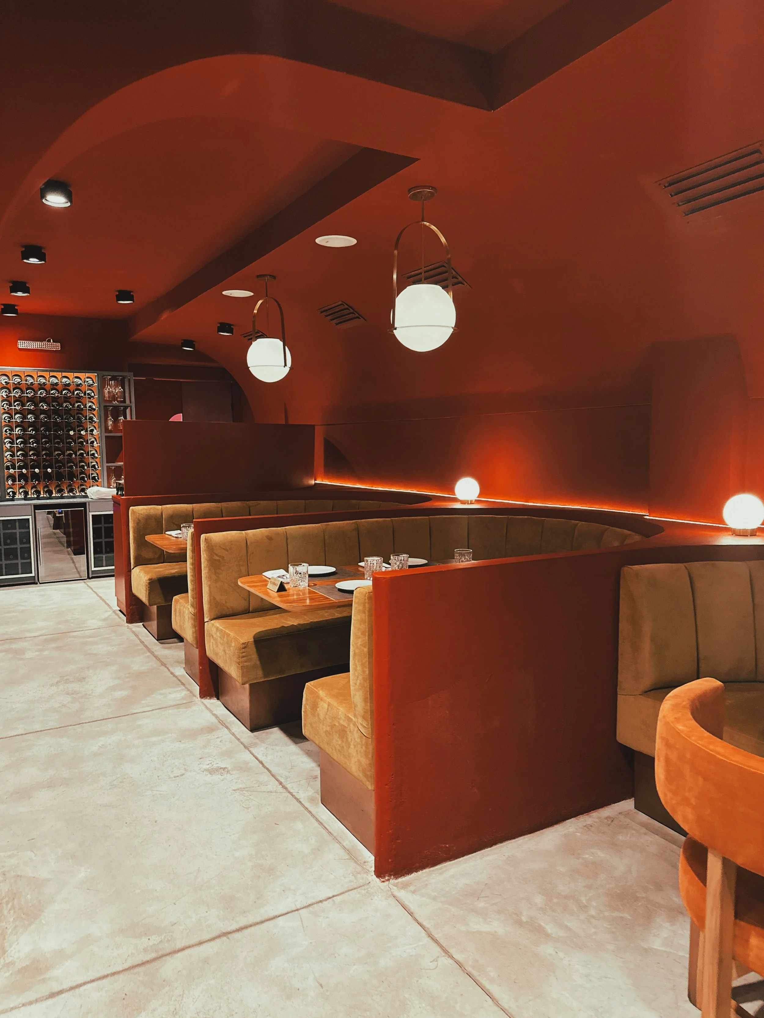 Zona de comedor en un restaurante con asientos de banqueta y mesas de madera, decorada con luces de bola colgantes y uvas en una cava trasera.