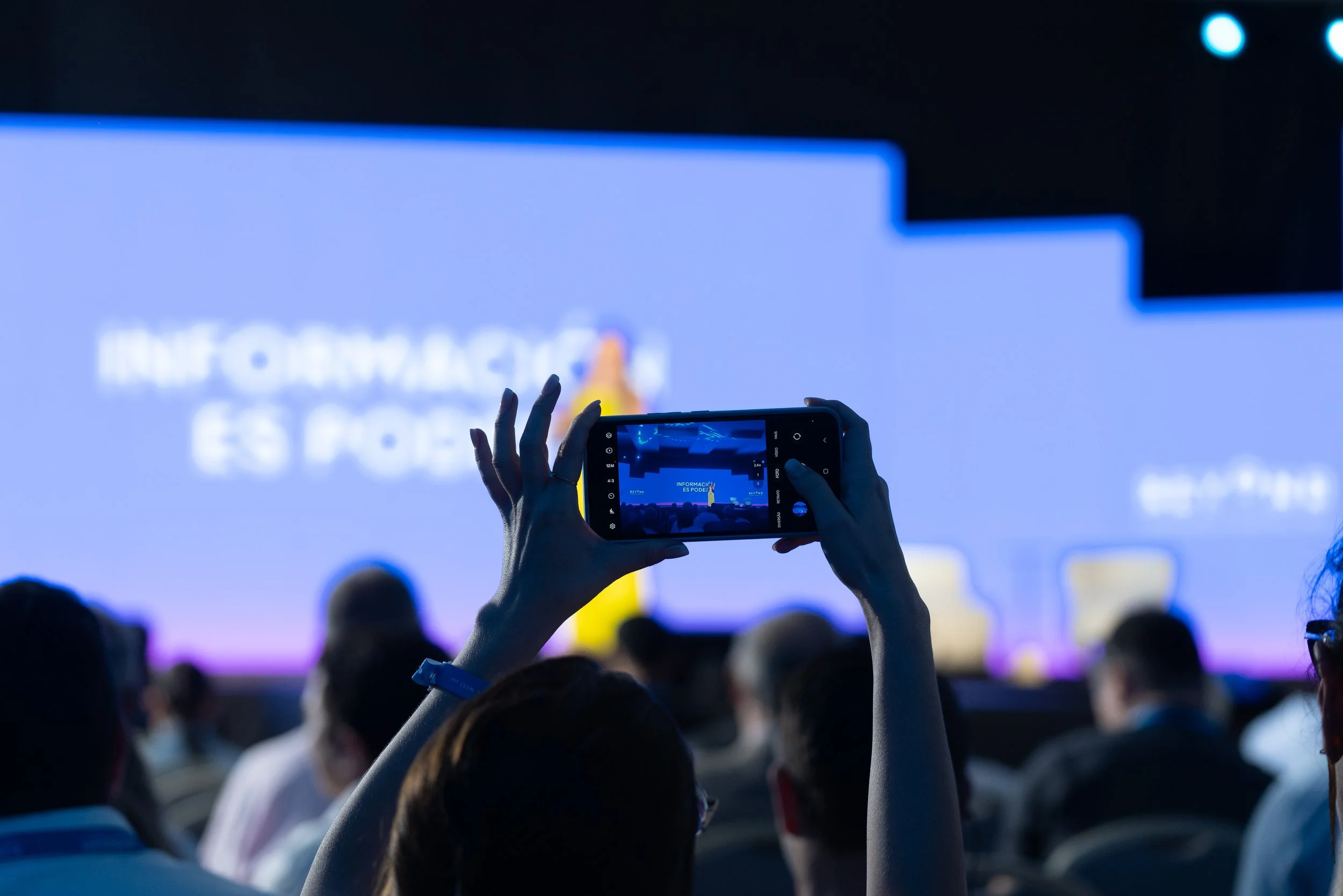 Persona tomando una foto de una pantalla grande en una conferencia o evento.