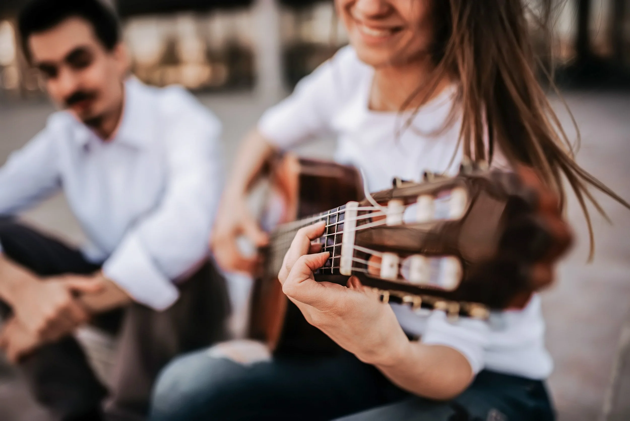 Personas tocando guitarra al aire libre, sonrisa, fondo borroso.
