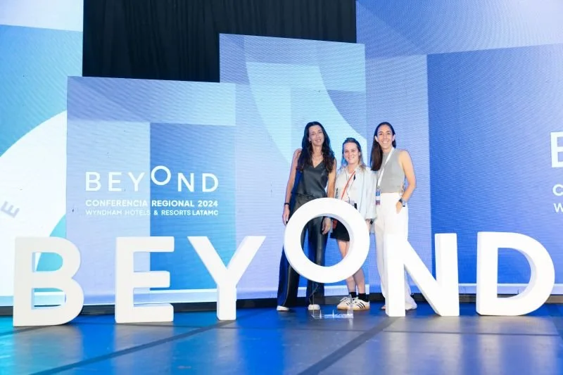 Tres mujeres son posando frente a un escenario con letras grandes que dicen 'BEYOND'.