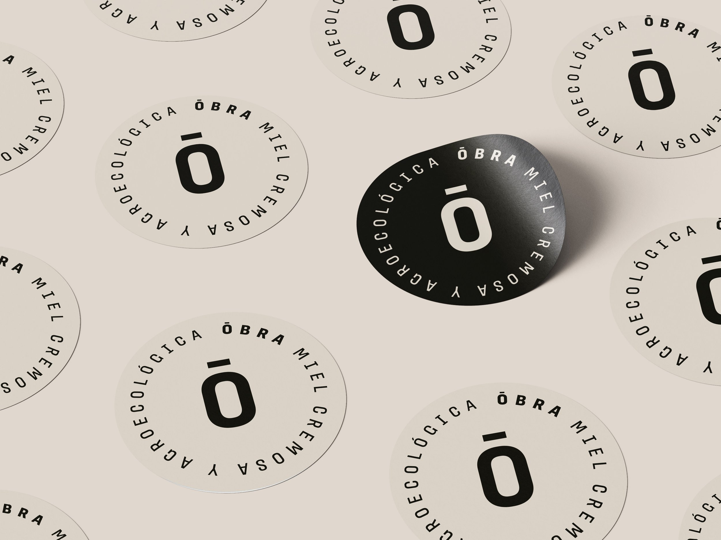 Logótipo circular en blanco y negro con la palabra 'ó' en el centro, rodeada de la leyenda en español 'Aduoecológica Óbra Miel Cremería'