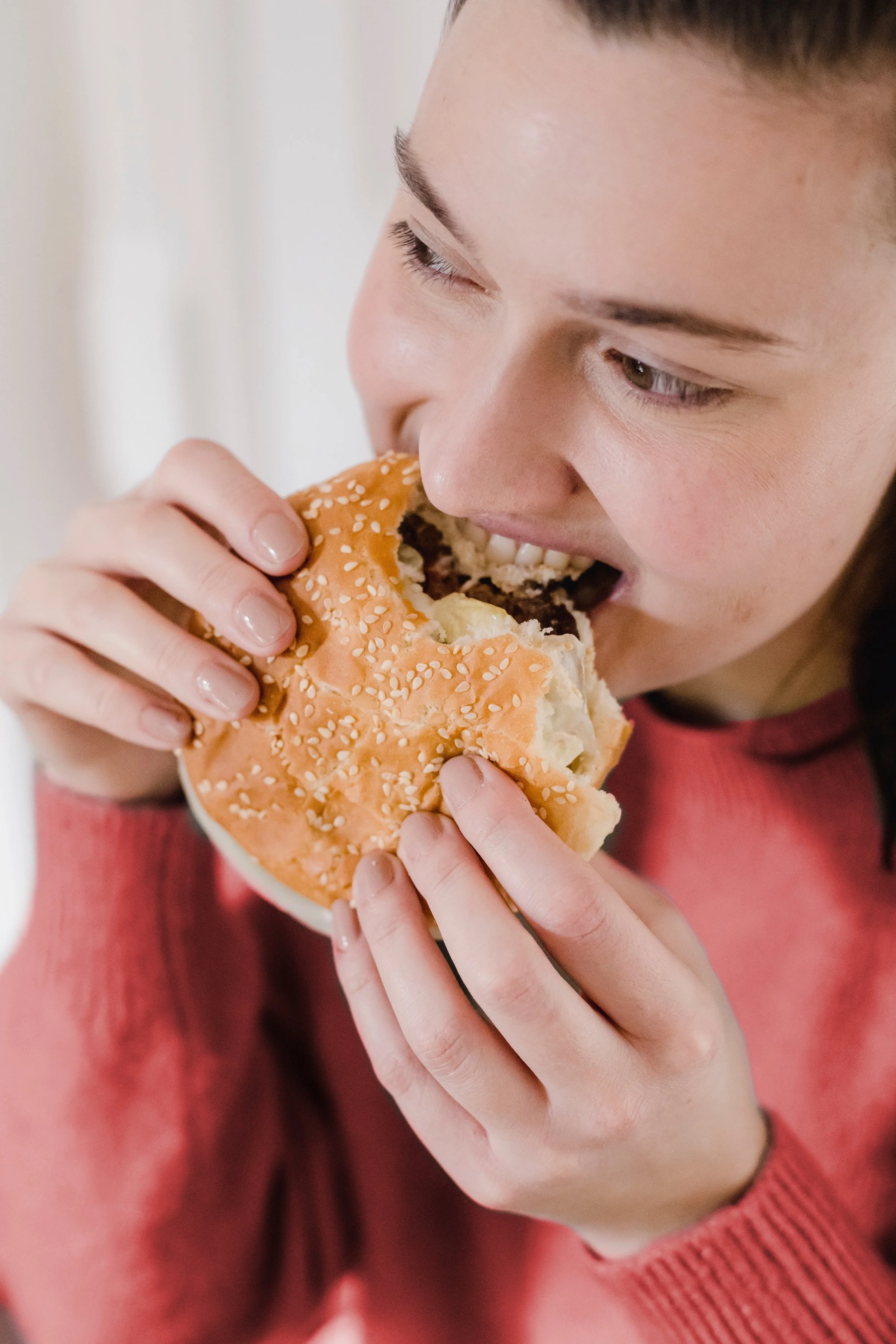 Joven comiendo una hamburguesa con pan con semillas de sésamo.
