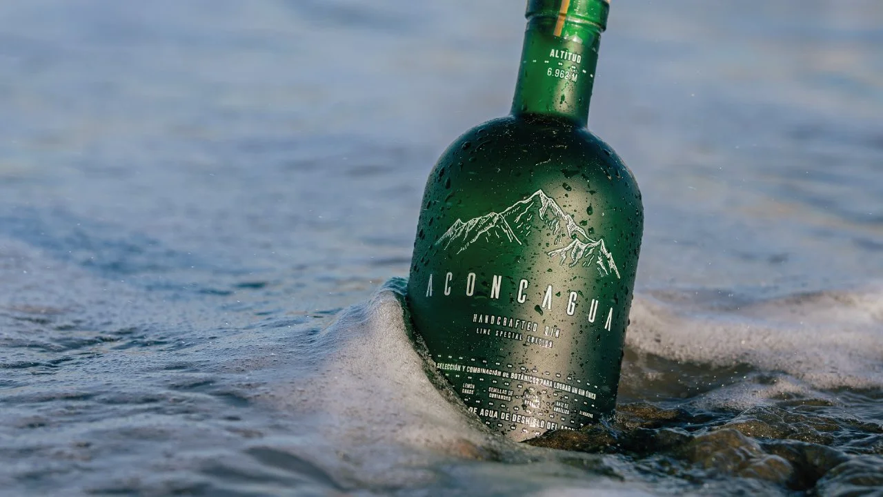 Botella de licor en agua con burbujas, con ilustración de montañas en la etiqueta.