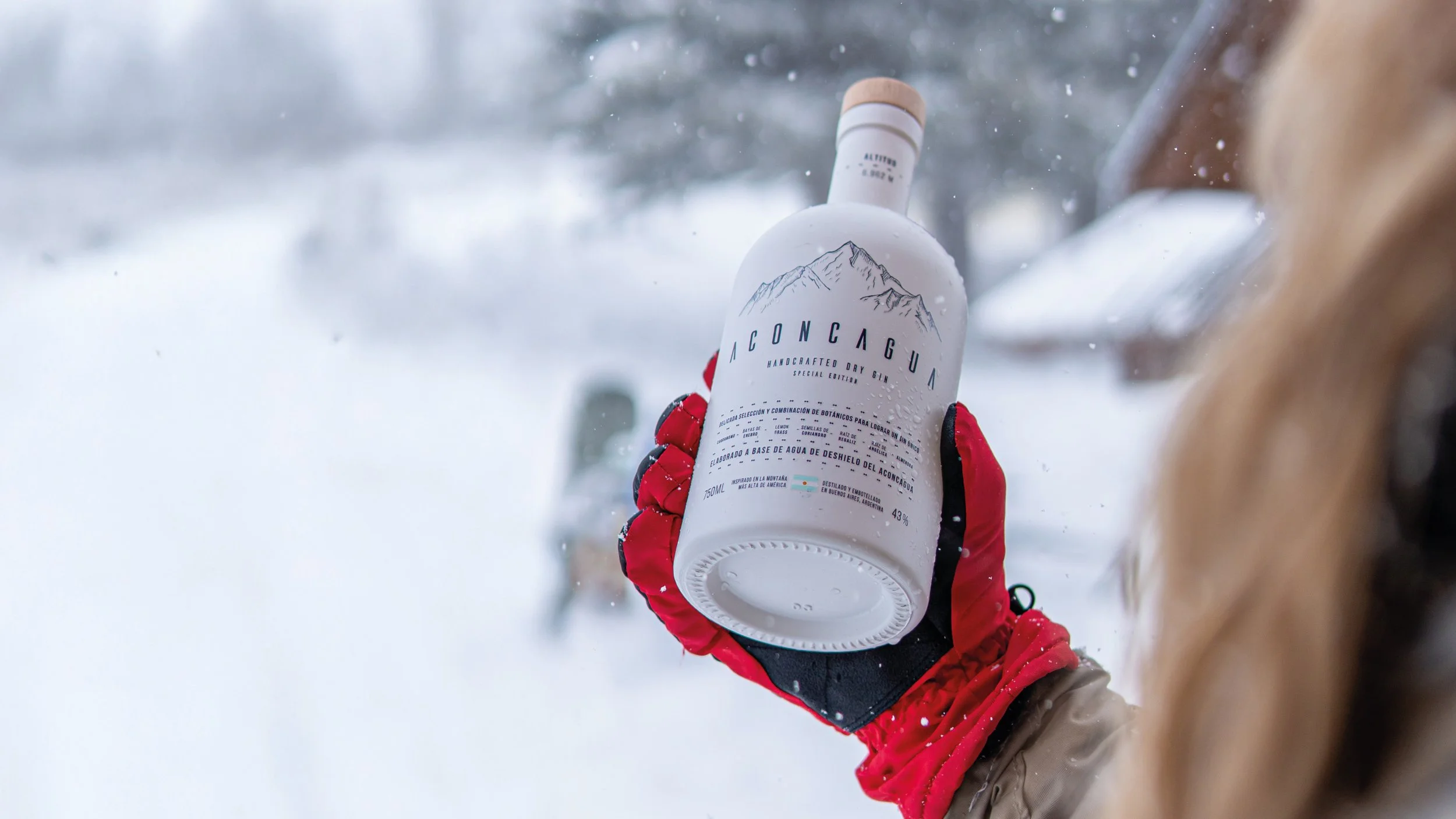 Persona con guantes rojos sostiene una botella de ginebra Aconcagua en un paisaje nevado.