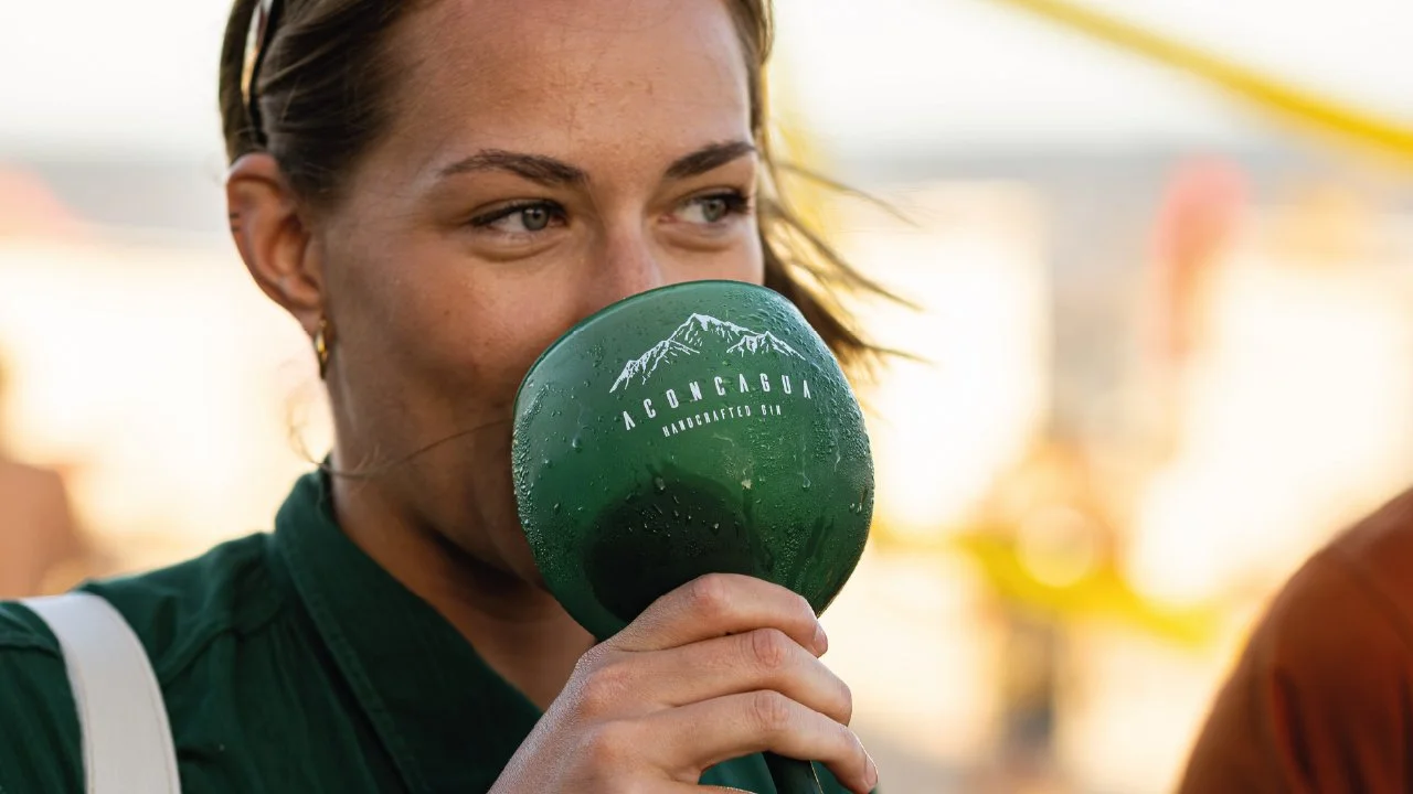 Mujer bebiendo desde una taza verde con logo que dice 'ACONCAGUA' y 'HANDCRAFTED CUBA', en un entorno exterior.