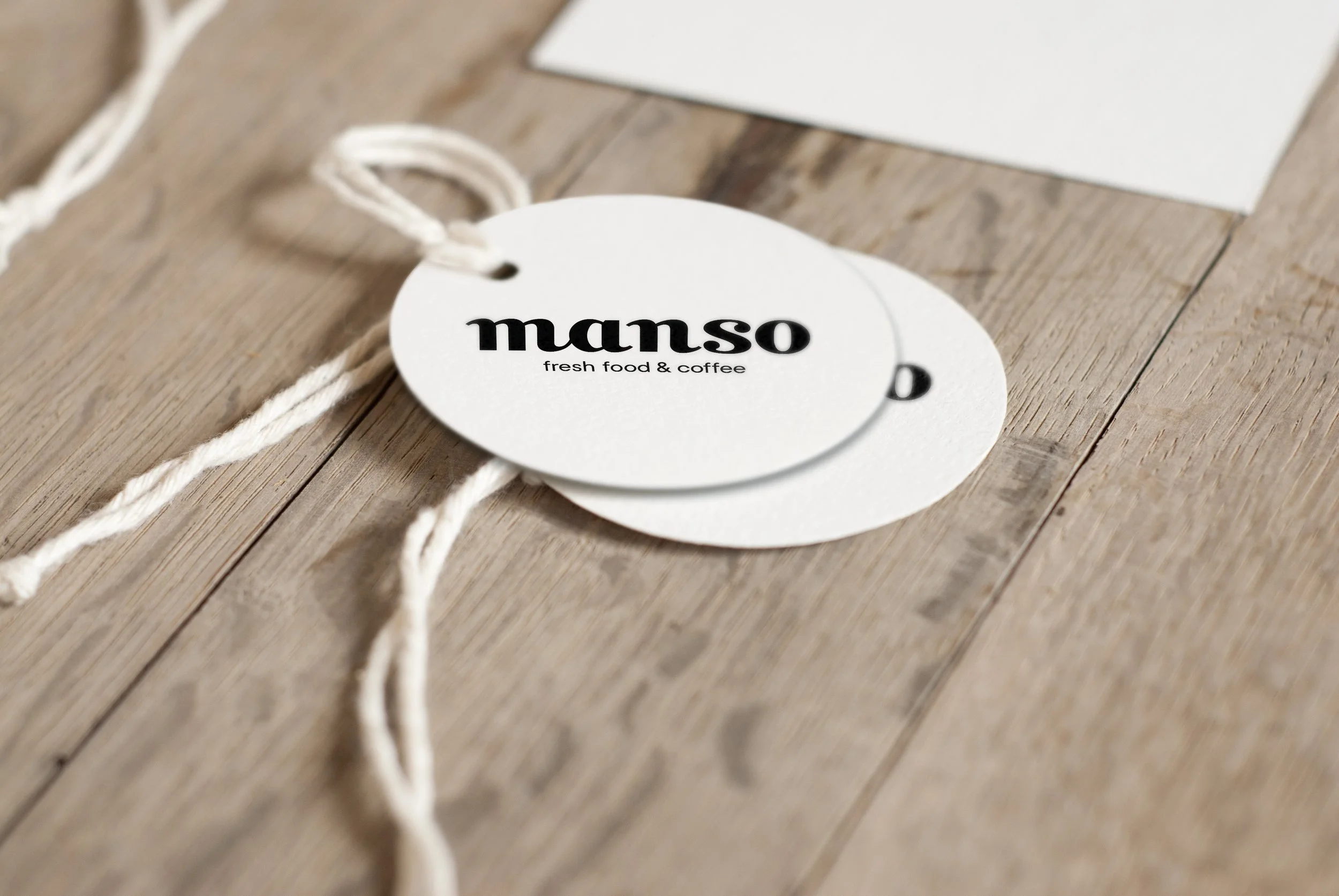Etiquetas blancas con la palabra 'manso' en letras negras y la descripción 'fresh food & coffee', colocadas sobre una superficie de madera