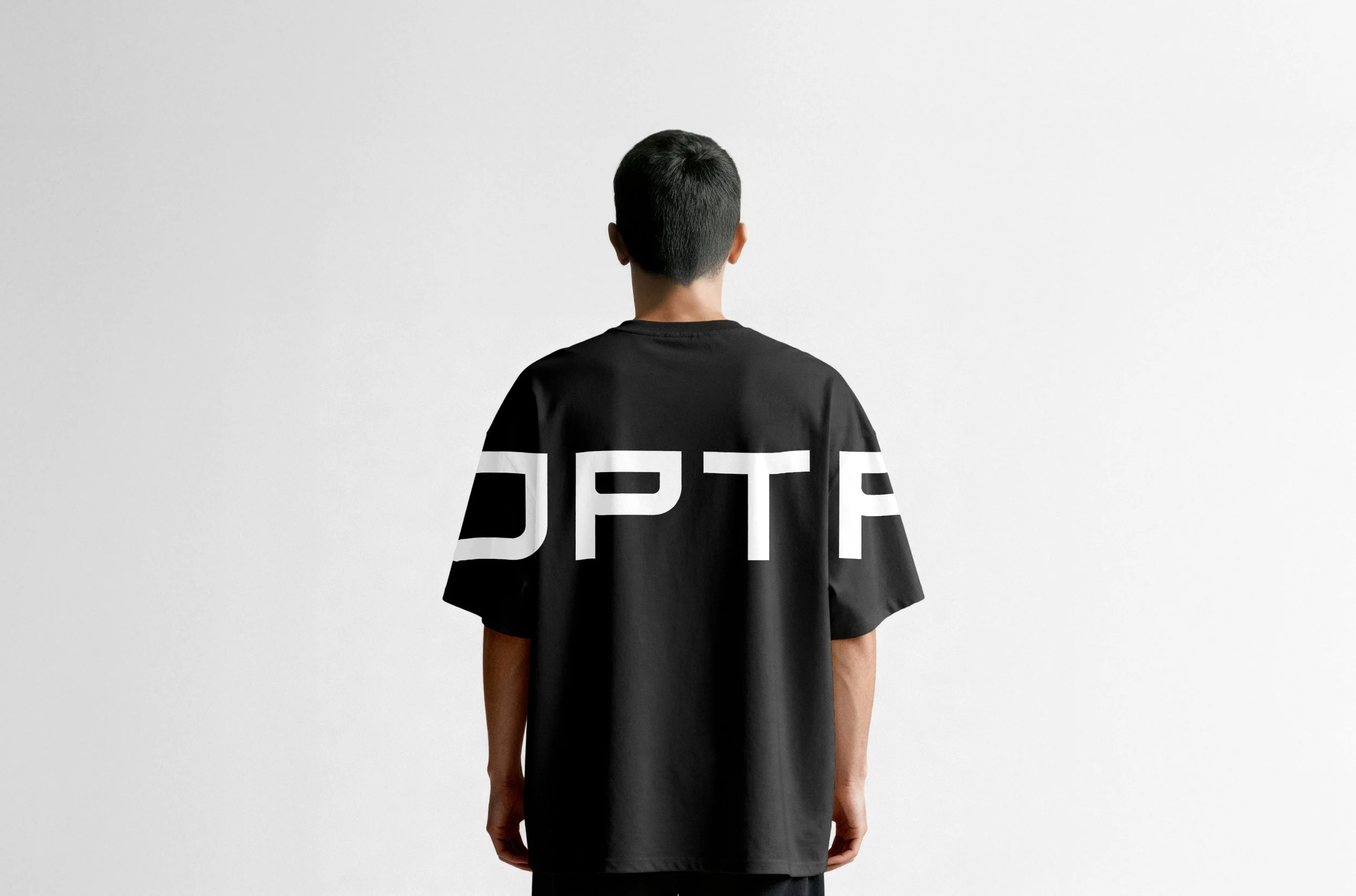 Joven con camiseta negra con letras blancas, vista desde atrás, en un fondo blanco