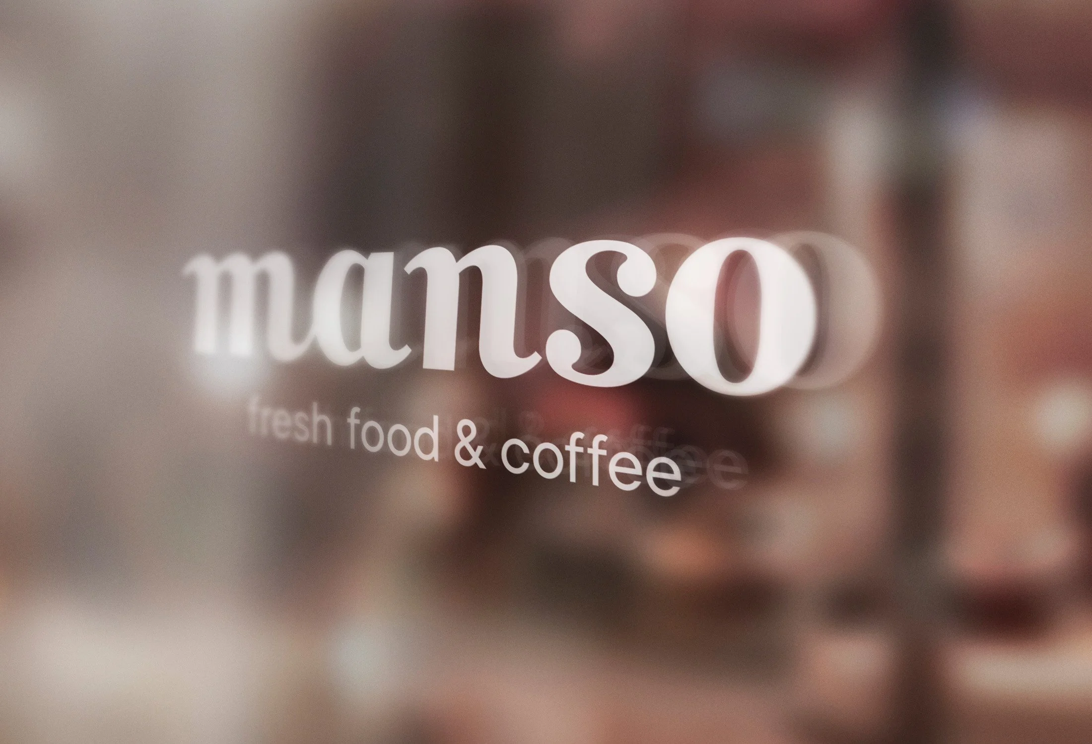 Texto que dice 'manso' y 'fresh food & coffee' en una superficie de vidrio, con un fondo difuso de colores cálidos.