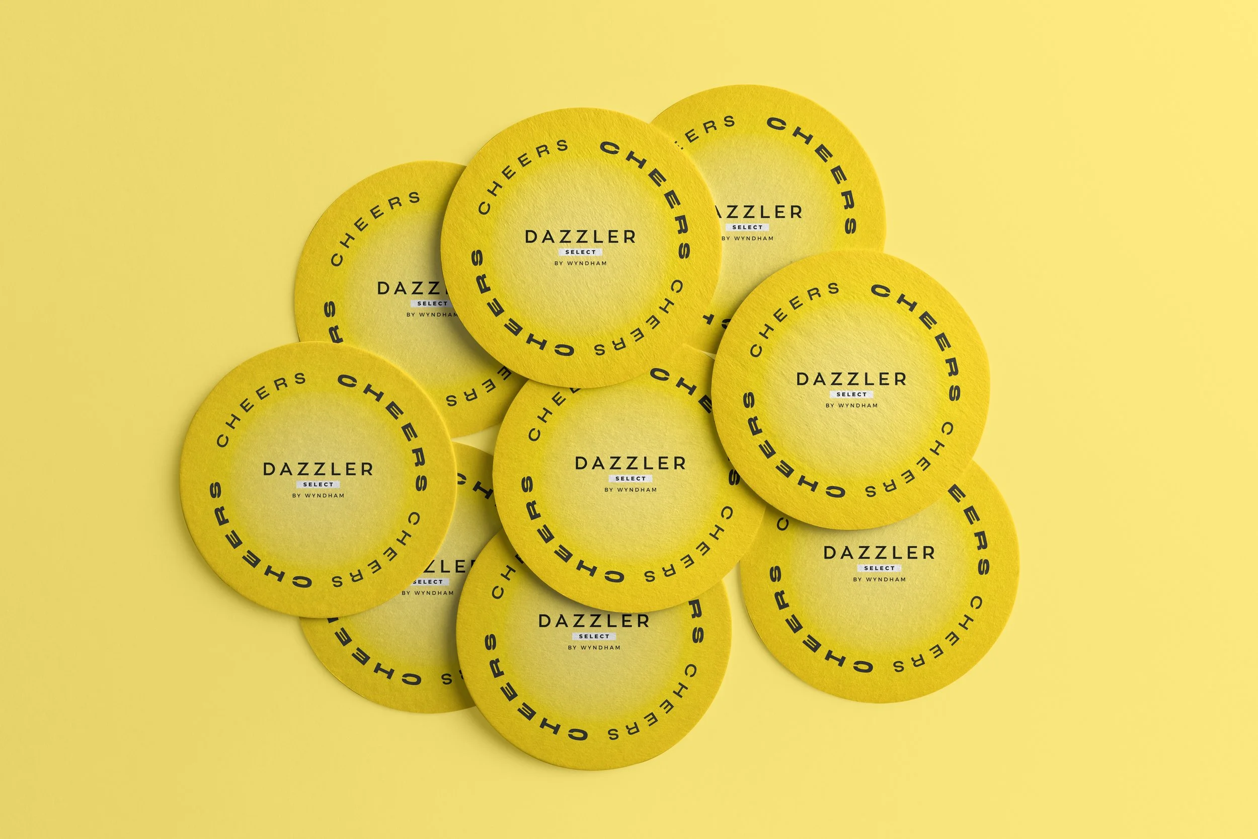 Carteles amarillos con la frase 'Cheers Cheer's' en un círculo, el texto 'DAZZLER SELECT BY WYNDHAM' en el centro, sobre fondo amarillo.