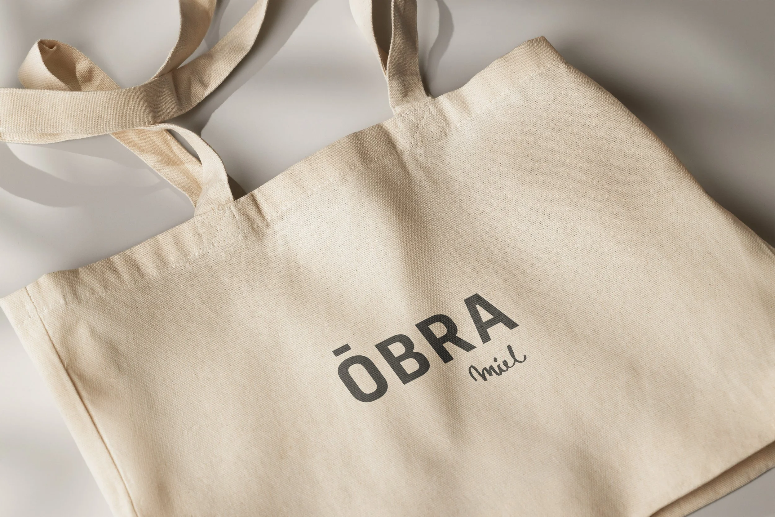 Bolsa de tela color crudo con la palabra ÓBRA en letras grandes y la palabra miel en un estilo de escritura más pequeño.