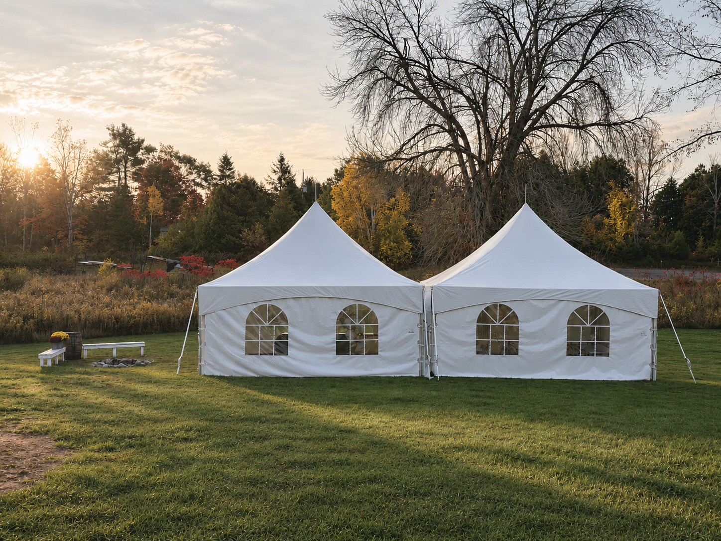 A white event tent set up on a grassy field during sunset, with trees and a partly cloudy sky in the background.