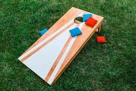 A cornhole game board with four bean bags on it is placed on grass.