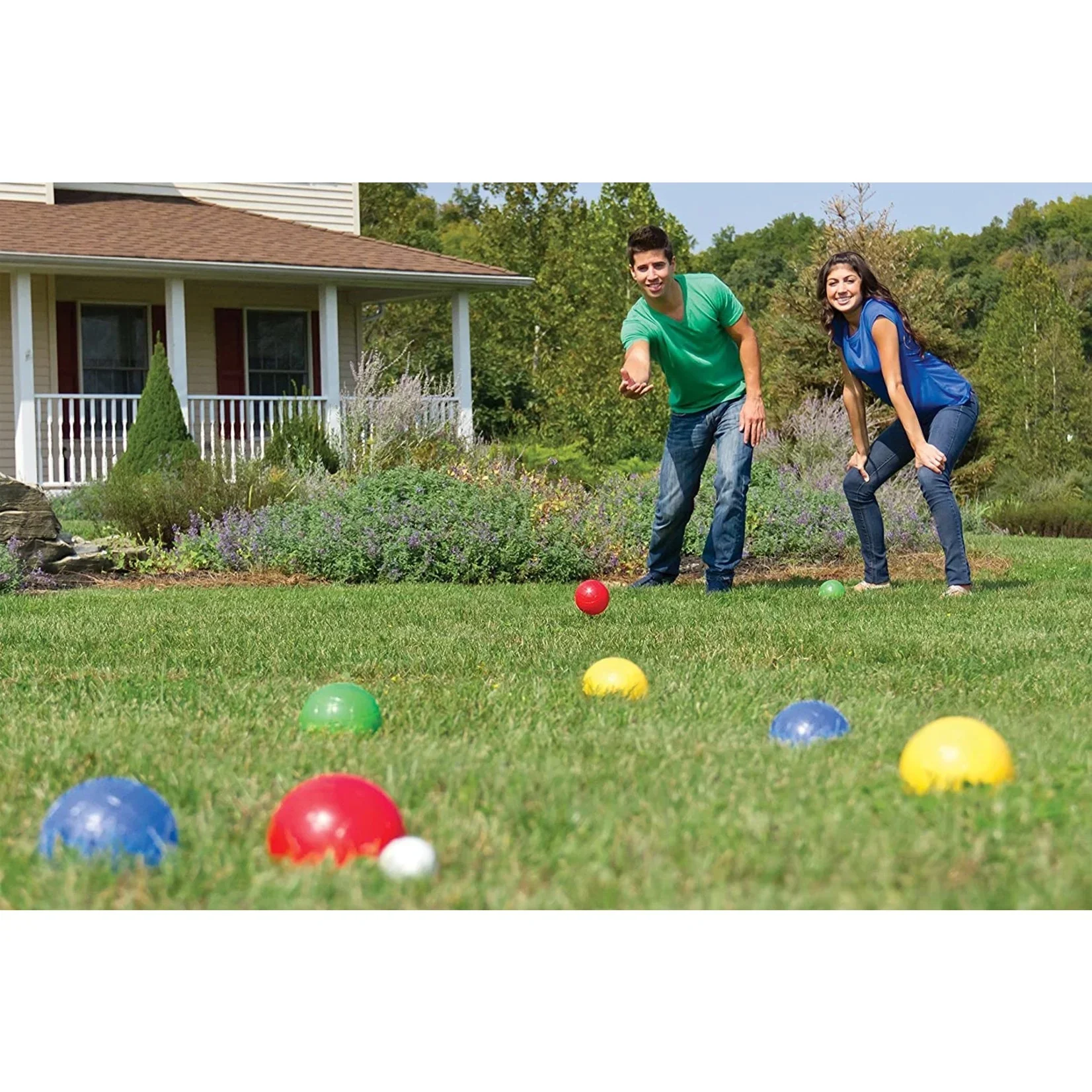 A young man and woman playing a game with colorful balls on a lawn in front of a house.