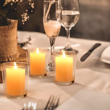 Three lit candles on a dinner table with glasses of water and a knife set in the background.