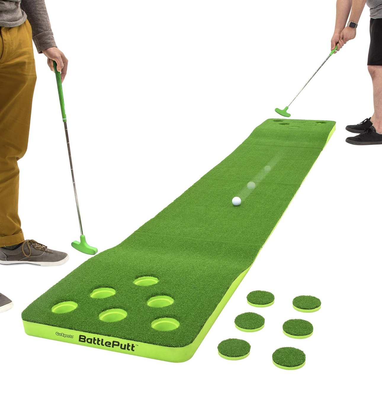 Two people playing mini golf on an indoor green mat with golf clubs and a golf ball. There are six holes on the mat and additional circular pieces on the side.