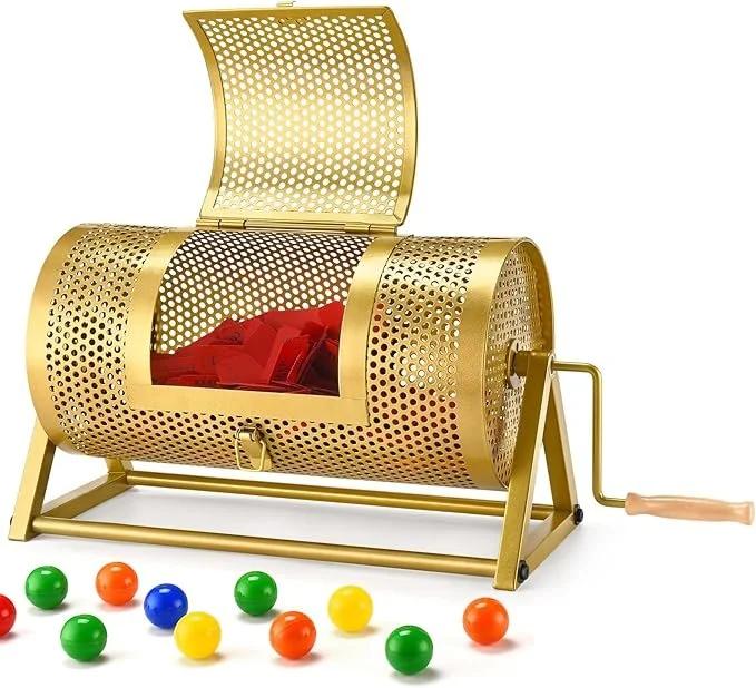 A gold-colored lottery drum with a handle, open lid revealing plastic balls inside, and additional colorful balls scattered in front.