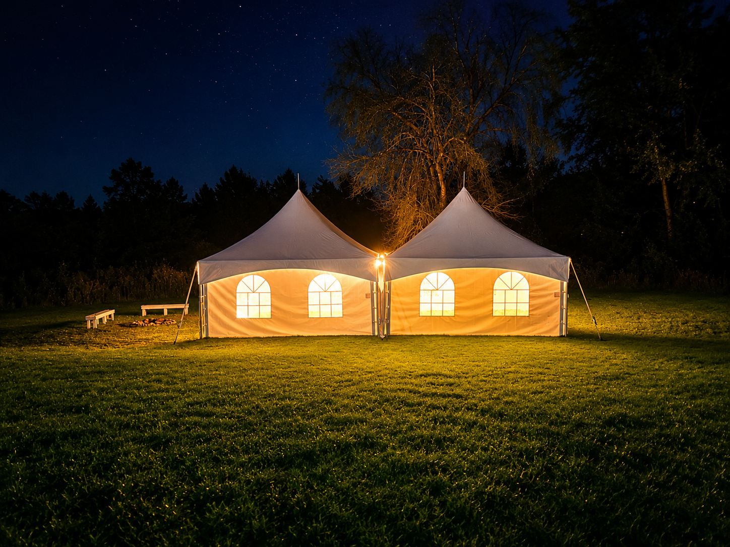 Two illuminated tents set up on a grassy field at night, with trees and a starry sky in the background.