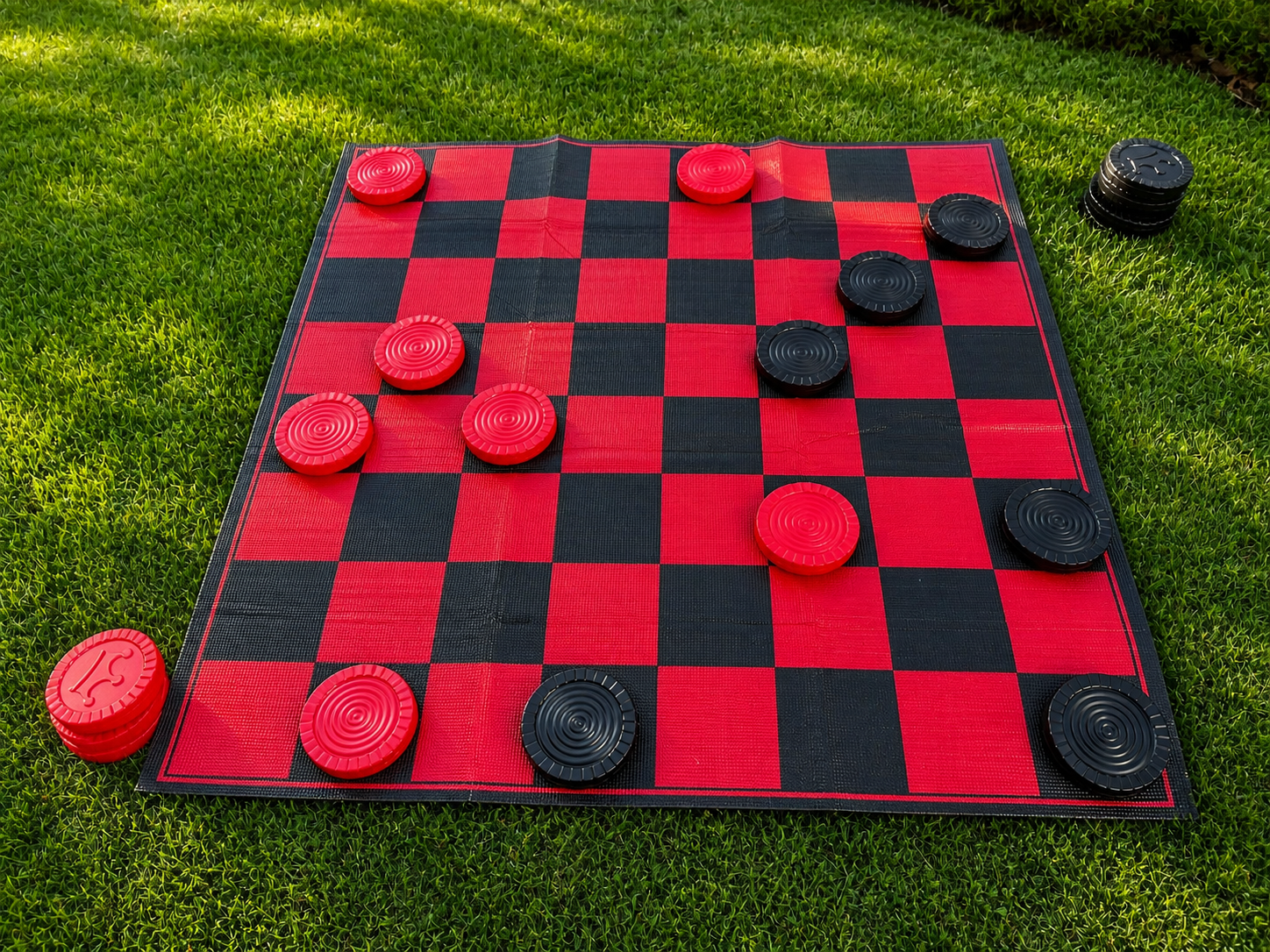 Checkers board game with red and black pieces placed on a grass lawn.