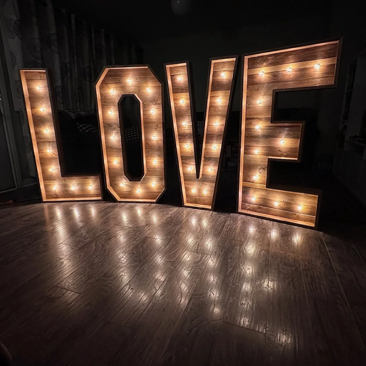 Large illuminated marquee sign spelling out the word 'LOVE' on a wooden floor in a dimly lit room.
