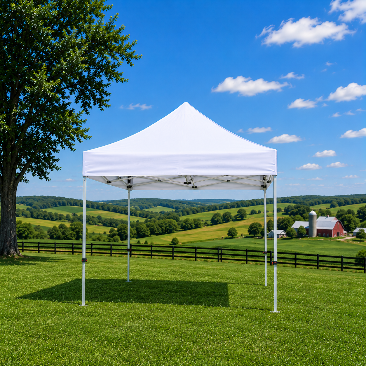 A white canopy tent set up on a grassy field with rolling green hills, farm buildings, and a blue sky with scattered clouds in the background.