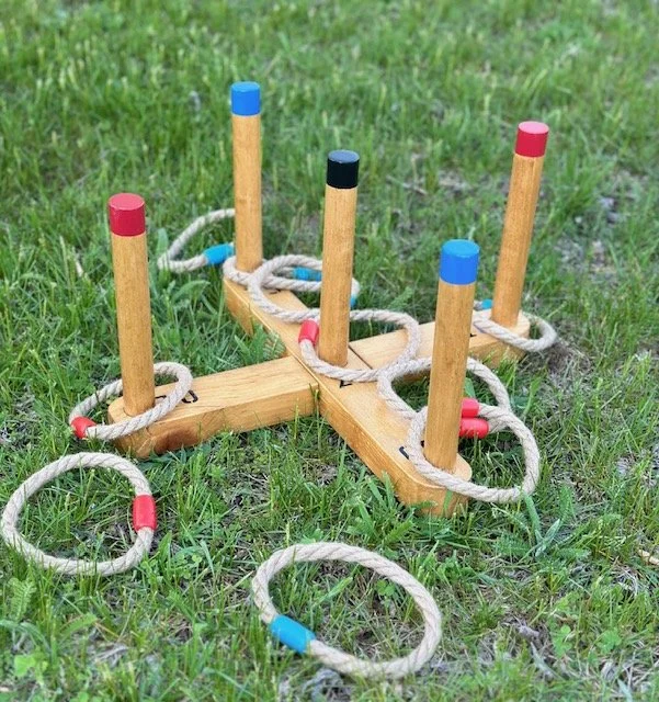 A wooden outdoor ring toss game with six colorful rings on a grassy lawn.