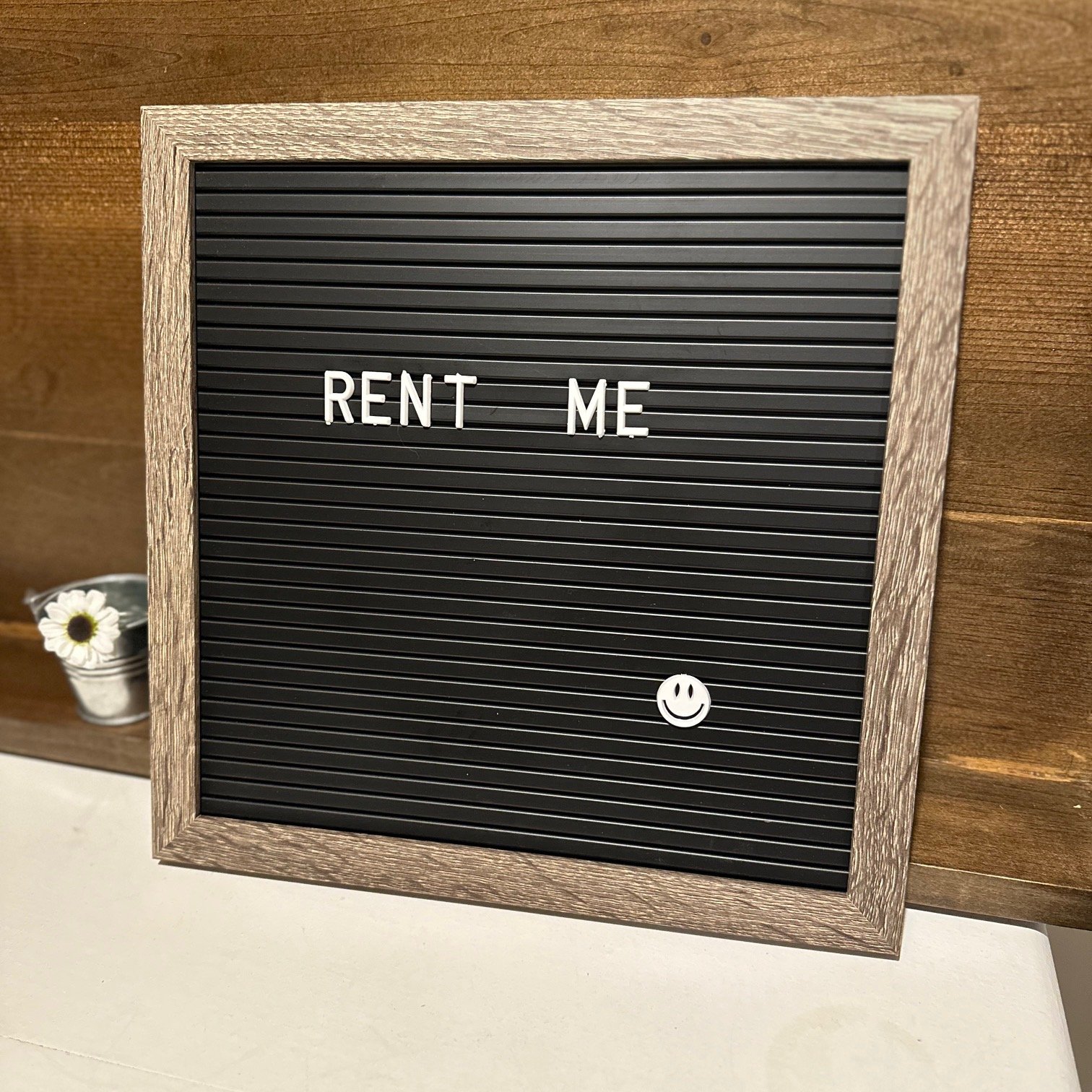 A black letterboard with the words "RENT ME" in white letters and a smiley face at the bottom right corner.