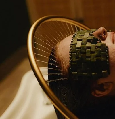 A person lying down with an arch of water jets receiving a Hair of the Catkskills Head Spa.