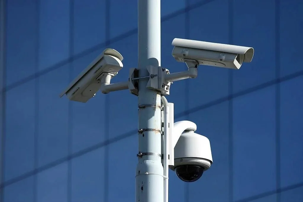 Security cameras mounted on a pole in front of a glass building.