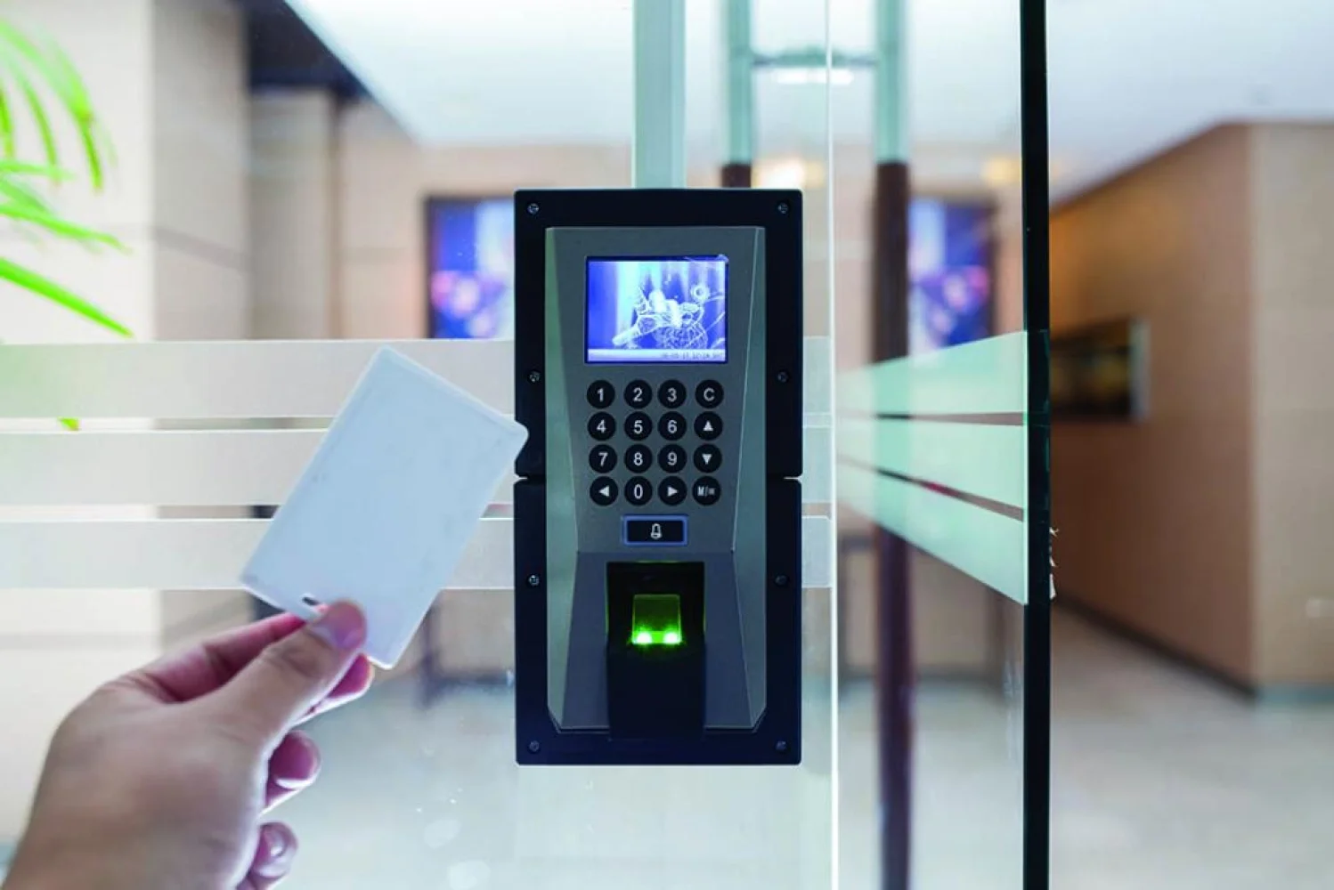 Person holding an access card near an electronic security turnstile or card reader in a building lobby.