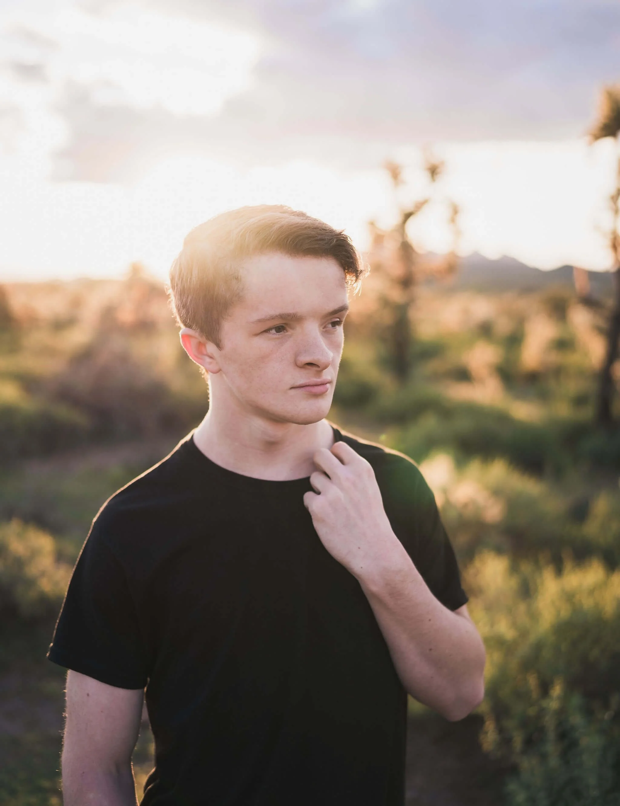 A young man tugging on his shirt during his senior photo session at Superstition Mountains