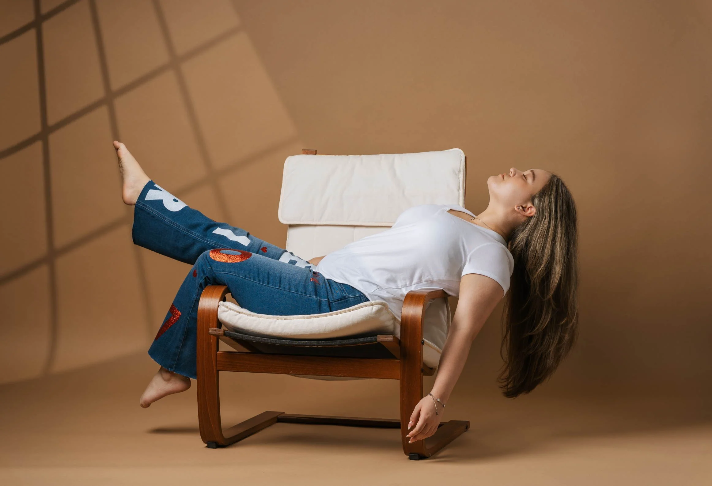 young woman sitting in a chair, kicking her leg up in front of an earthy toned backdrop